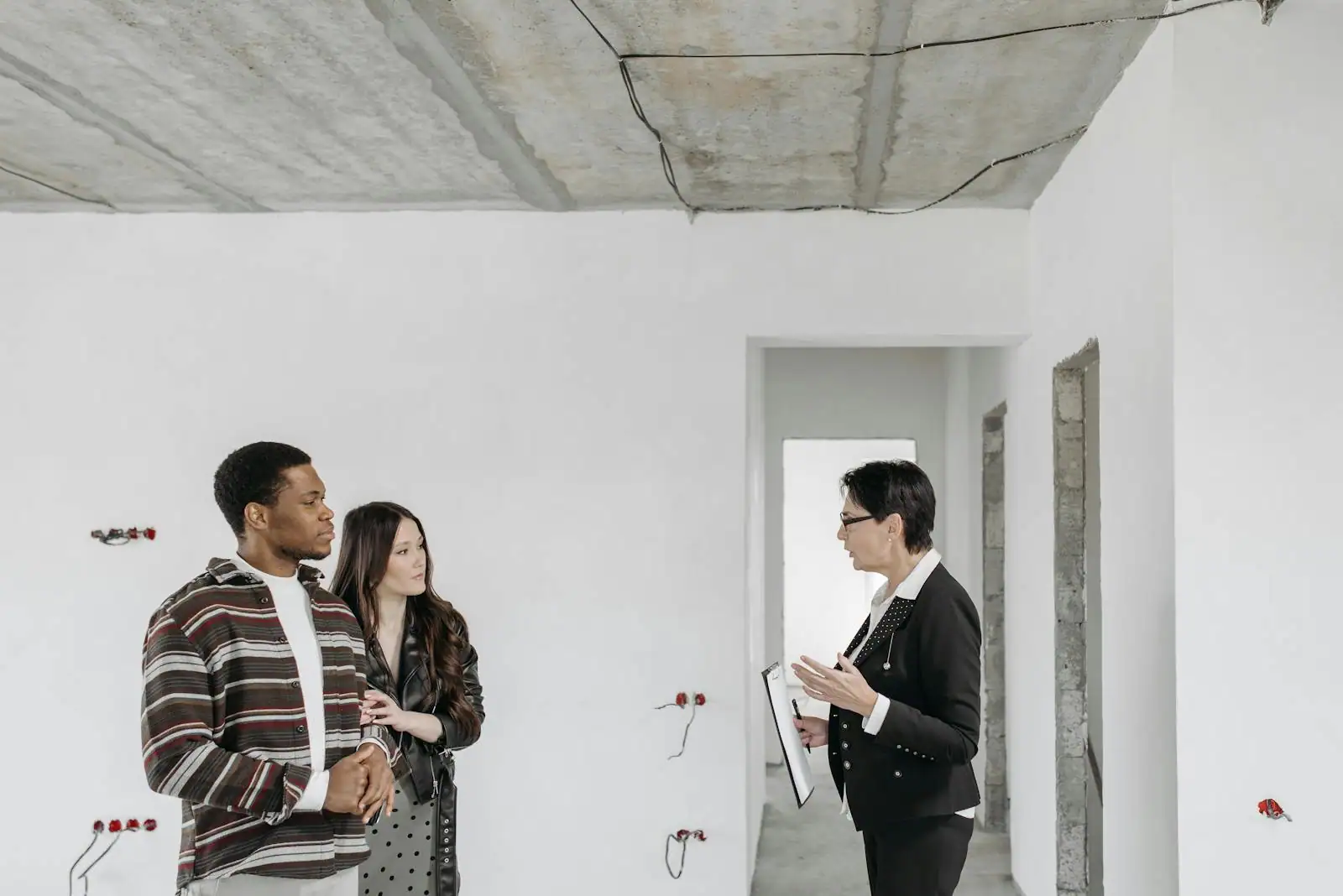 Couple visitant un appartement vide avec un agent immobilier, lumière naturelle par les fenêtres