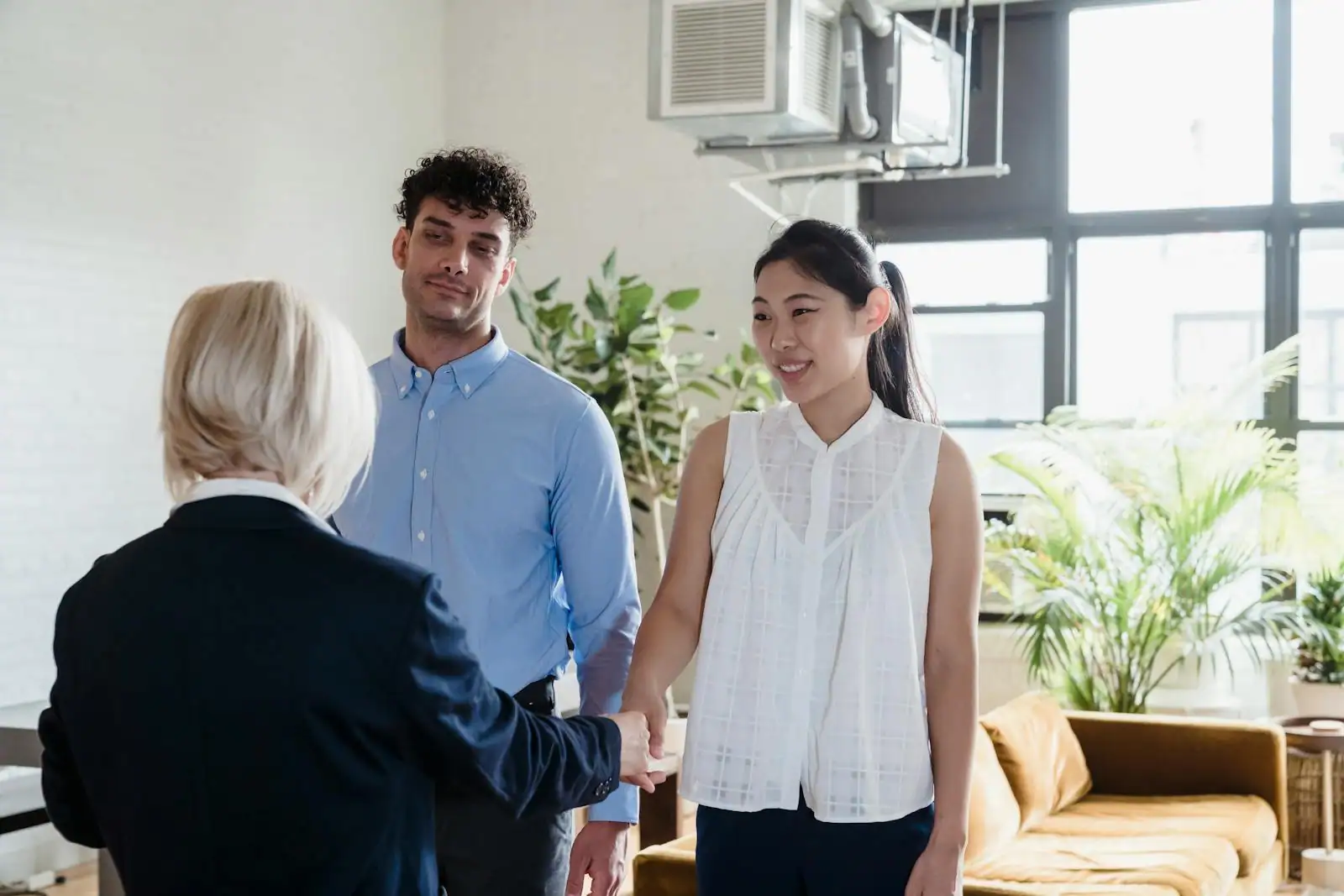 Couple visitant un appartement parisien lumineux avec un agent immobilier, plans posés sur une table en bois
