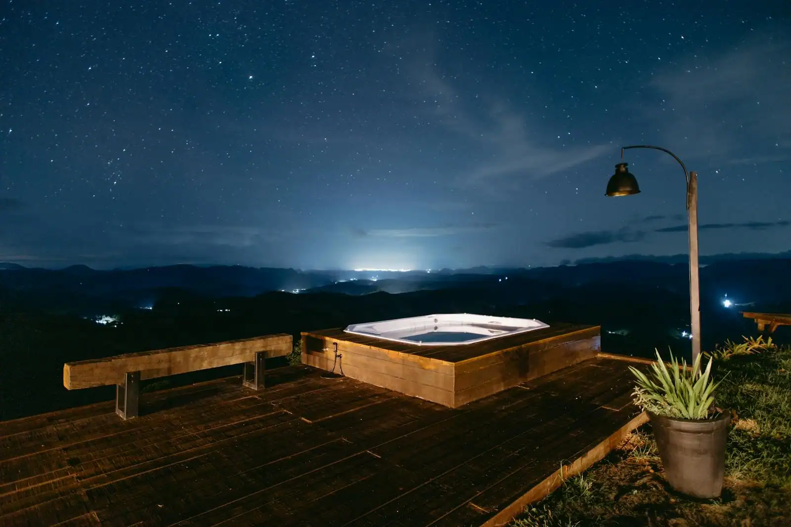 Spa de jardin encastré dans terrasse bois avec brise-vue végétal et éclairage indirect chaud en soirée
