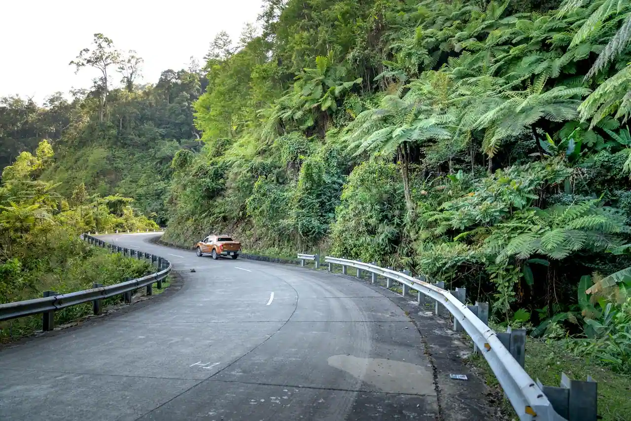 Voiture garée sur une route côtière de Guadeloupe avec vue sur la mer des Caraïbes et la végétation tropicale.