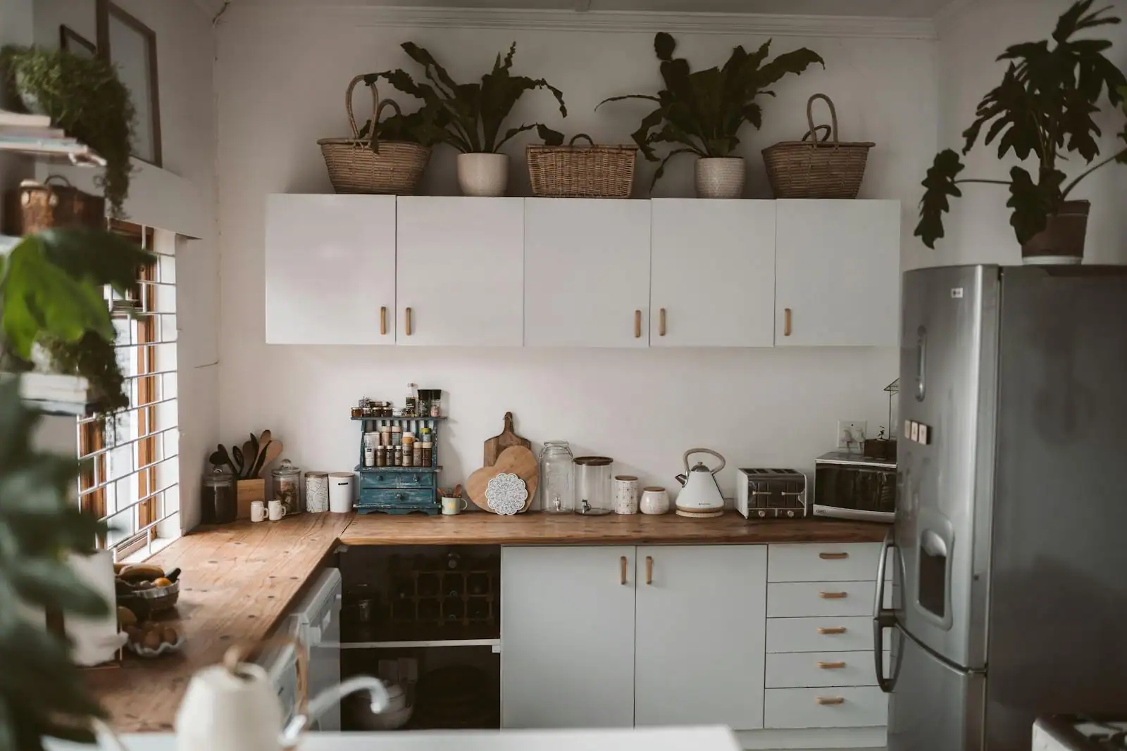 Cuisine contemporaine avec meubles blancs mats, plan de travail en bois clair et crédence en zellige vert sauge sous lumière naturelle