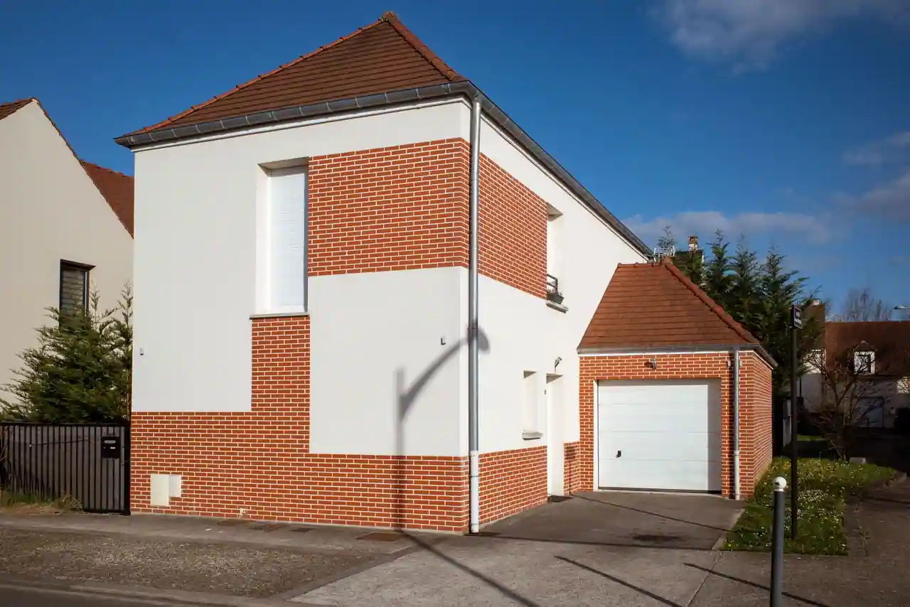 Maison individuelle moderne à la façade mêlant enduit blanc et briques rouges, avec garage attenant