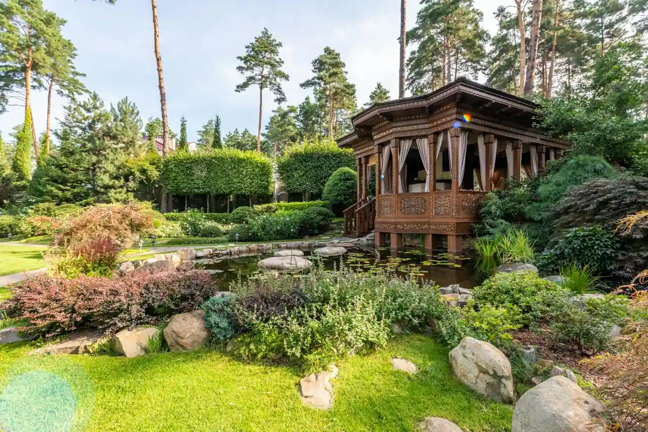 Jardin paysager avec un kiosque en bois au bord d'un bassin, entouré de rochers et de massifs de plantes