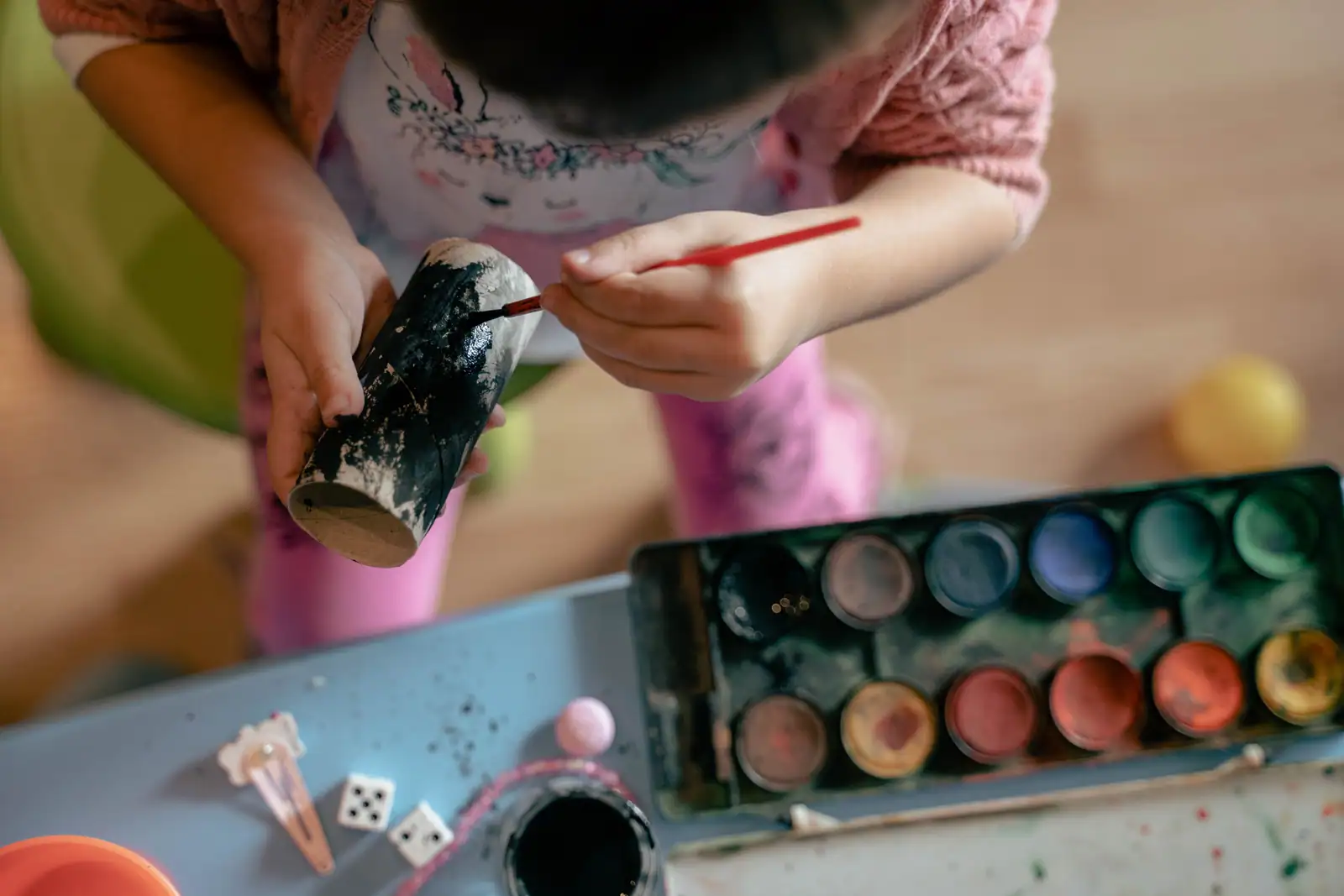Enfant peignant un rouleau en carton avec un pinceau, près d'une palette de peinture