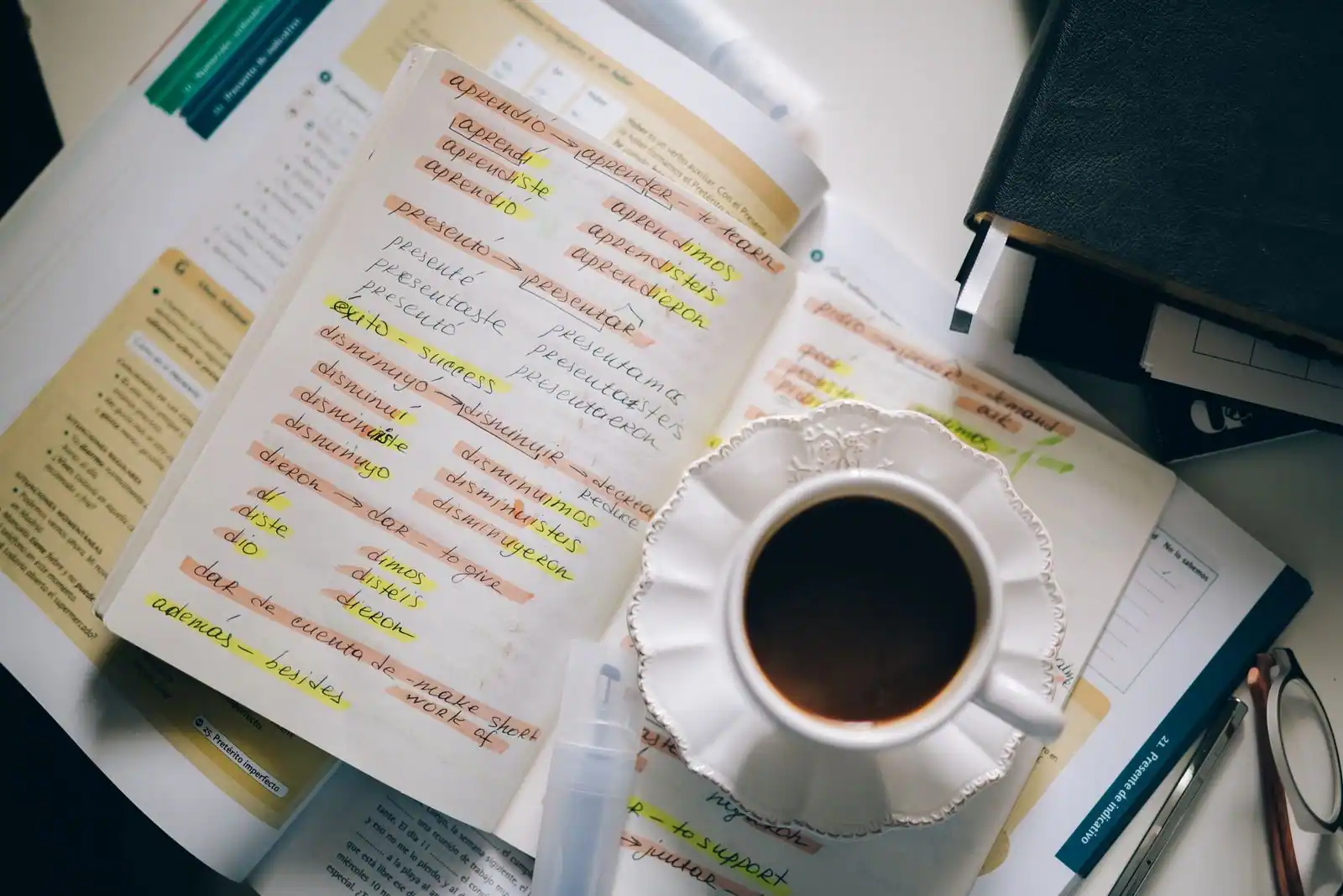 Notes manuscrites d'espagnol et manuels de conjugaison sur un bureau, avec une tasse de café, scène d'apprentissage
