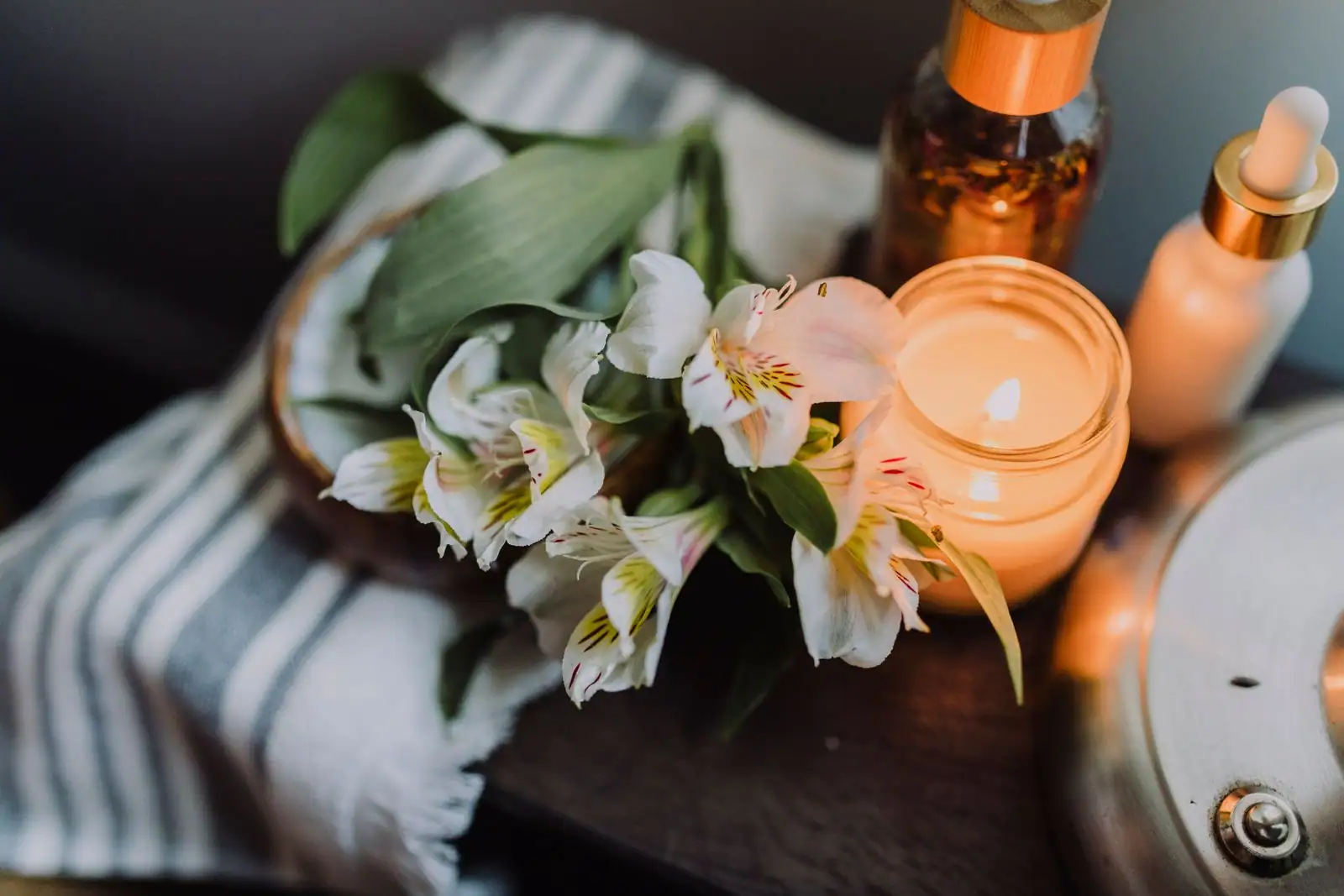 Fleurs blanches et bougie allumée disposées sur une table en bois, ambiance douce et sobre