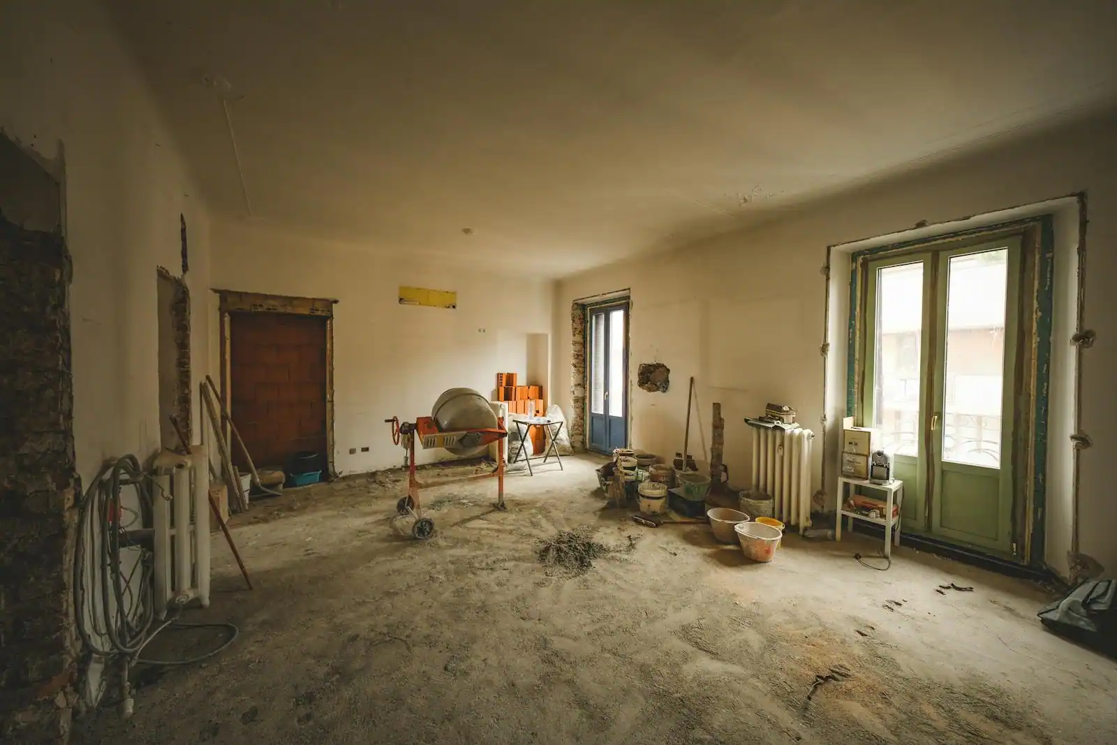 Pièce de maison en cours de rénovation, murs décapés et bétonnière au milieu d'un sol poussiéreux