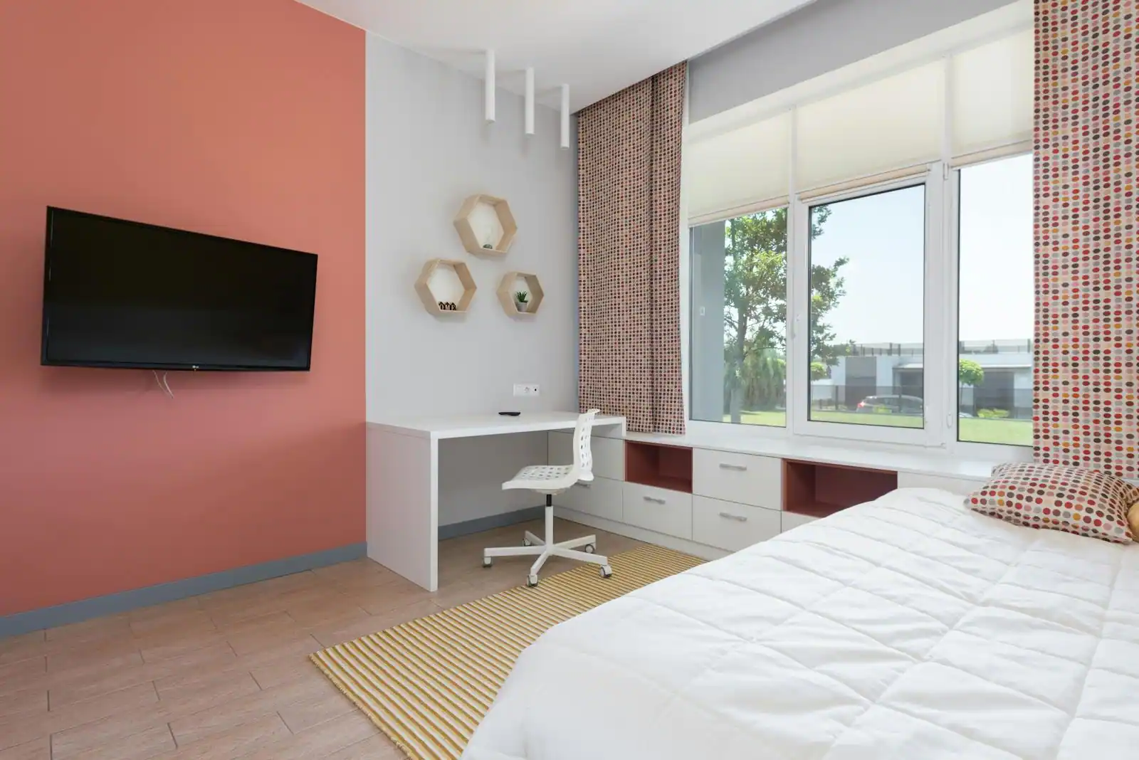Chambre lumineuse avec un bureau et sa chaise, des étagères murales hexagonales et un mur orange corail