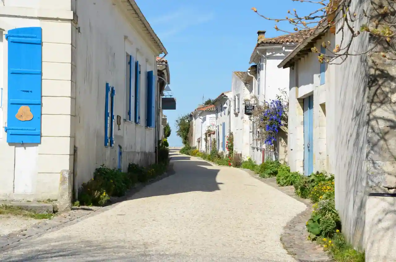 Ruelle pavée d'un village côtier bordée de maisons blanches aux volets bleus et de massifs fleuris