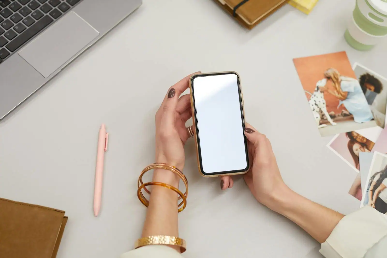 Personne tenant un smartphone moderne devant un ordinateur portable, en train de comparer des offres en ligne
