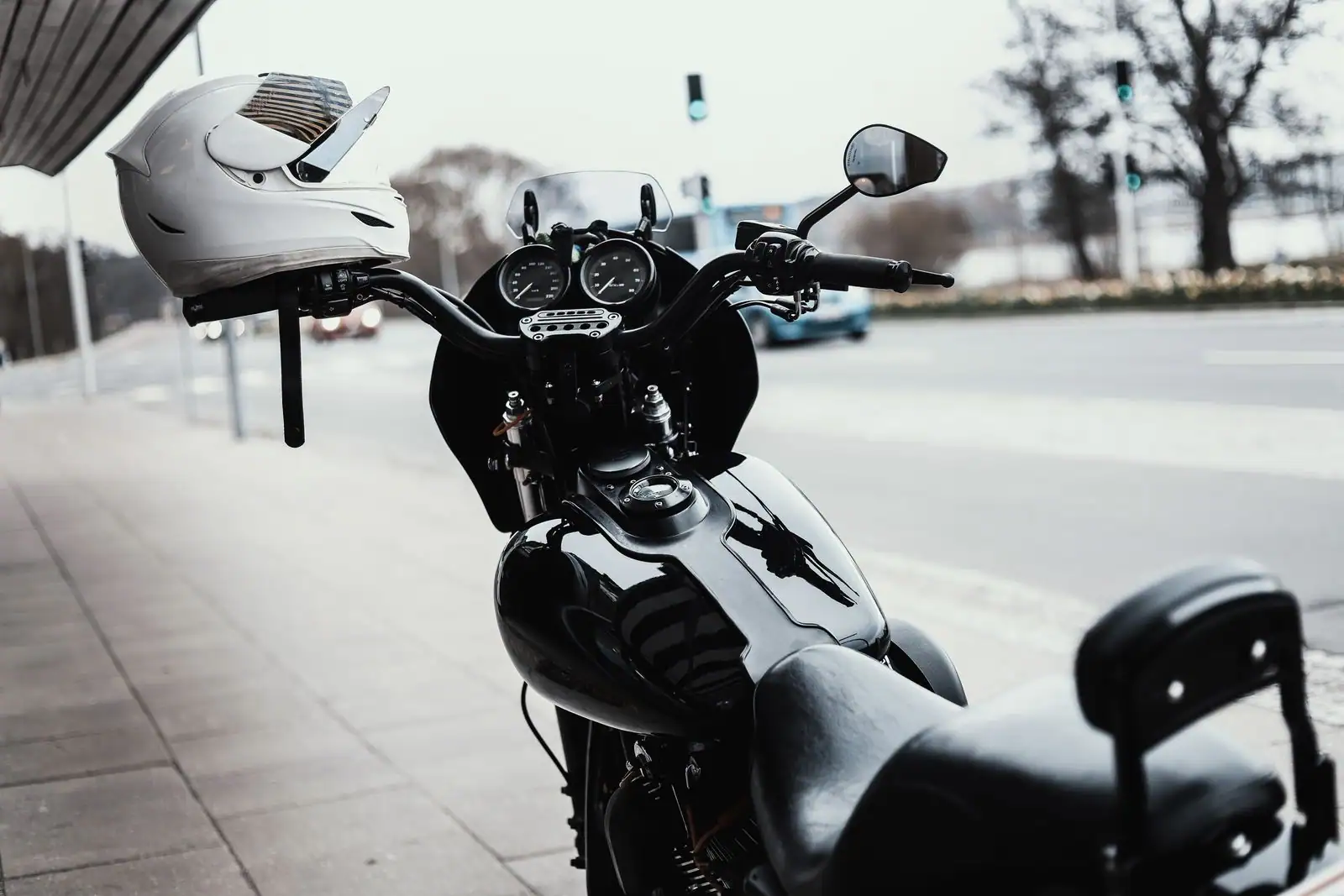 Moto noire garée le long d'un trottoir en ville, un casque blanc accroché au guidon, prête pour une location.