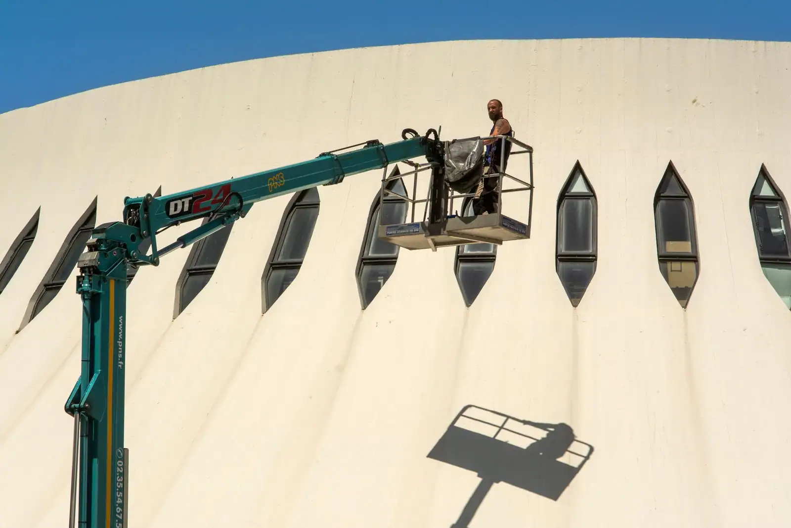 Ouvrier dans la nacelle d'une plateforme élévatrice à bras, déployée en hauteur le long d'une façade