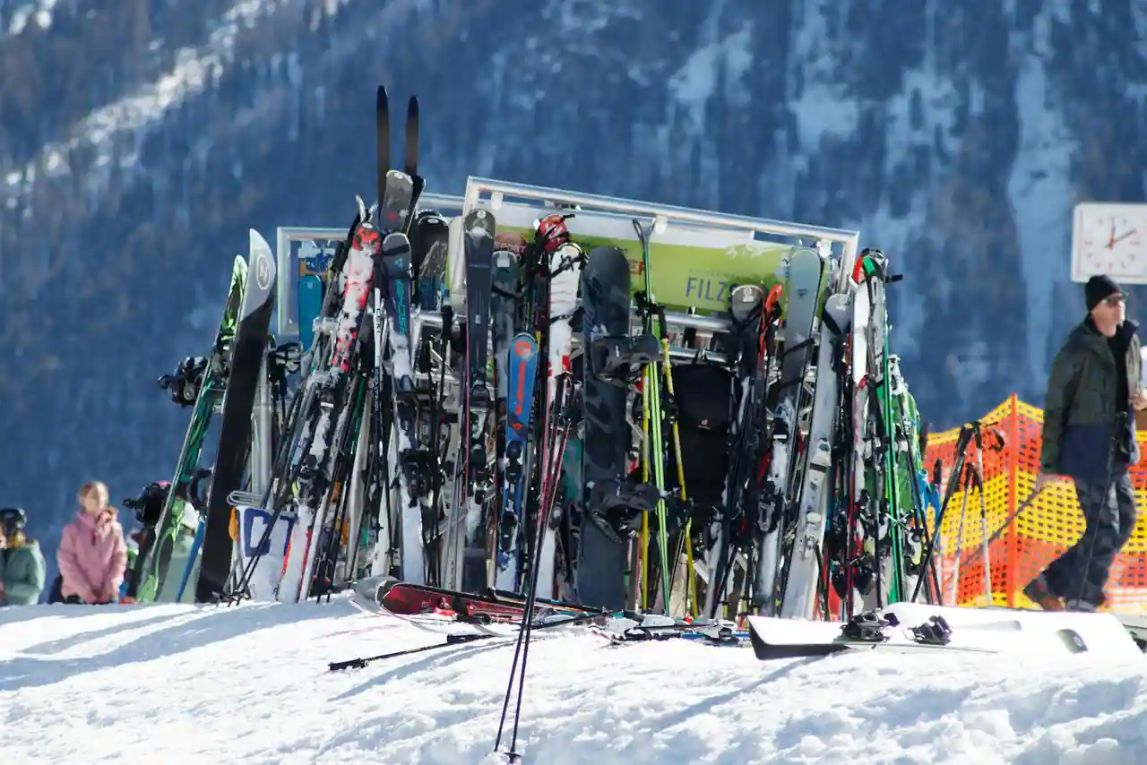 Skis et snowboards rangés sur un râtelier métallique extérieur, sur la neige d'un domaine skiable de montagne