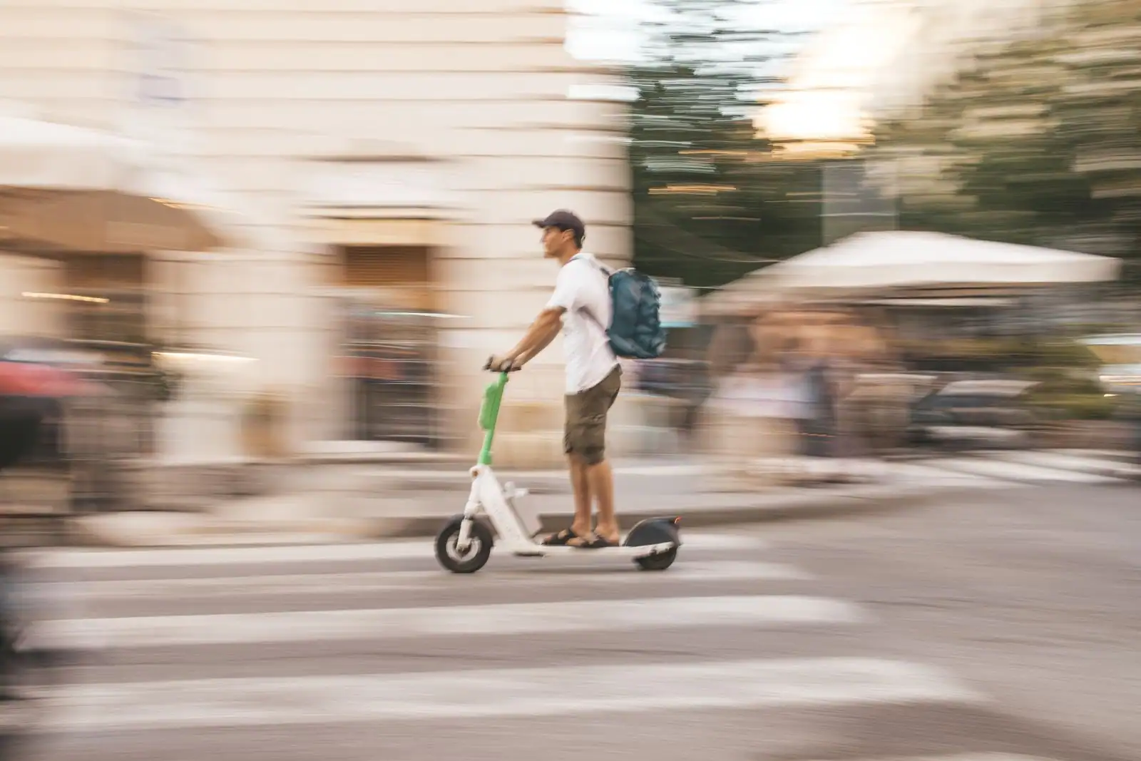 Un homme se déplace à trottinette électrique dans une rue de ville, un sac sur le dos, en pleine circulation