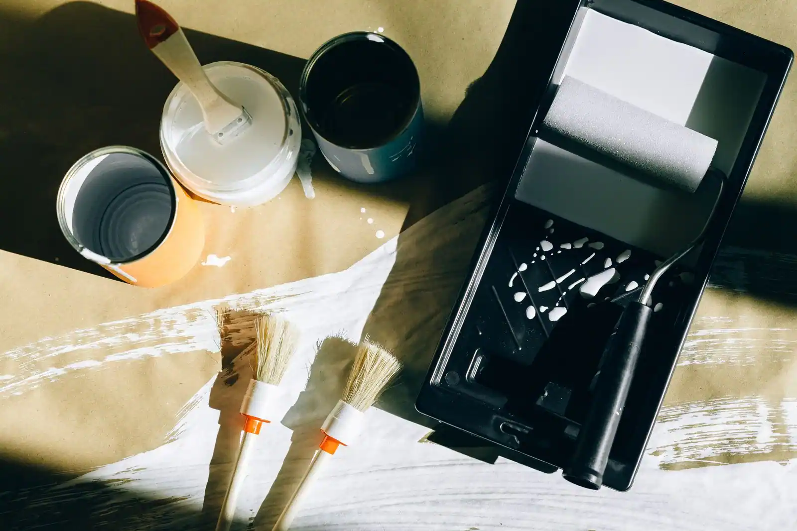 Pots de peinture, pinceaux et rouleau de bricolage posés sur une bâche de protection