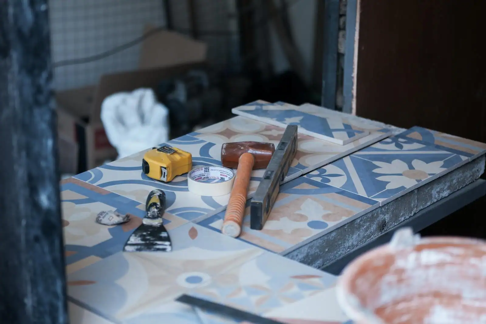 Outils de carreleur posés sur des carreaux à motifs : mètre ruban, maillet, niveau et spatule, sur un chantier