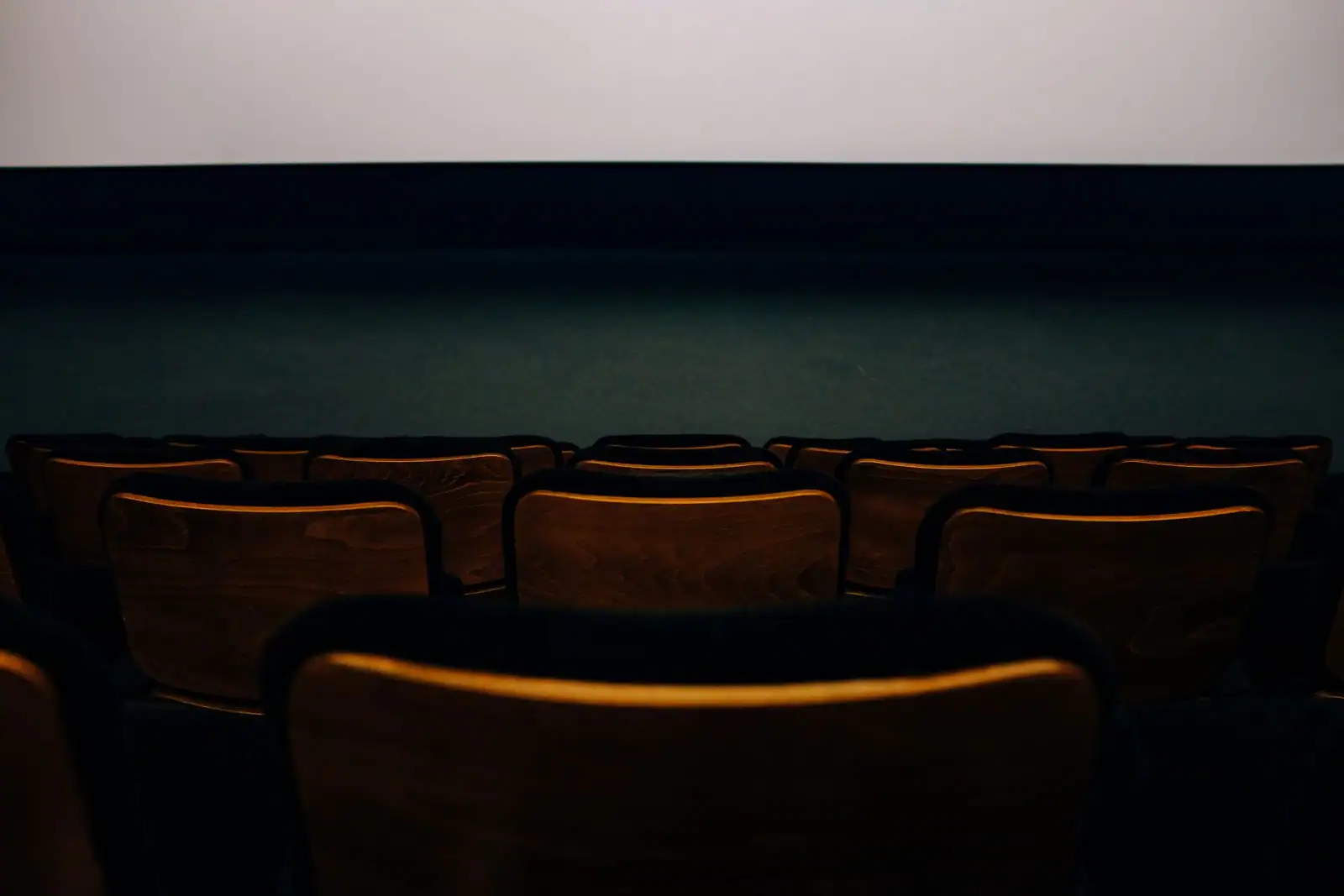 Rangées de sièges en bois vides dans une salle de cinéma, face à l’écran éclairé