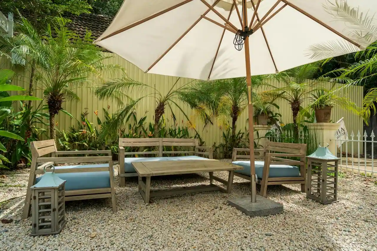 Salon de jardin en bois grisé : banquettes, fauteuils et table basse sous un parasol sur une terrasse