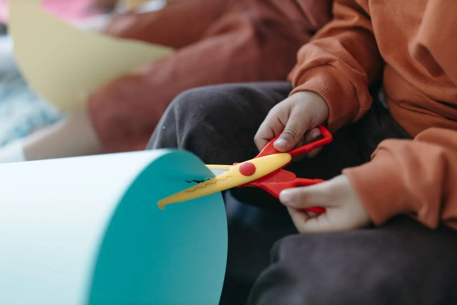 Mains d'enfant découpant du papier coloré avec des ciseaux à bouts ronds pendant un atelier de bricolage.
