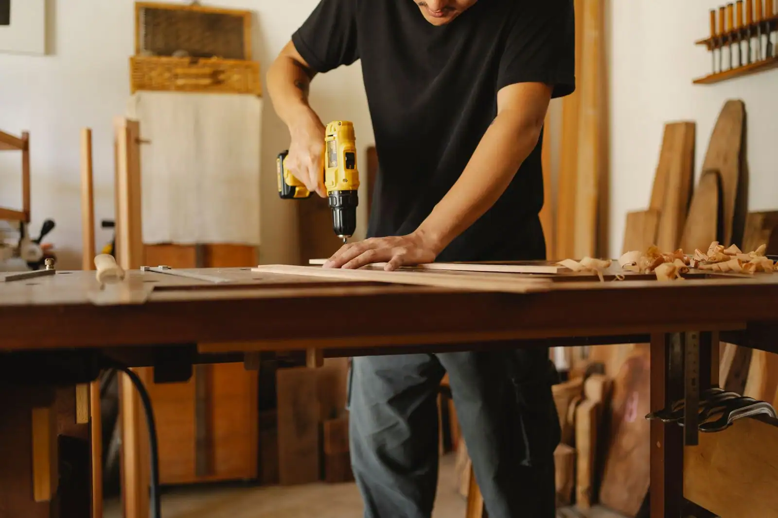 Une personne perce une planche de bois à la perceuse sans fil sur un établi, dans un atelier de bricolage.