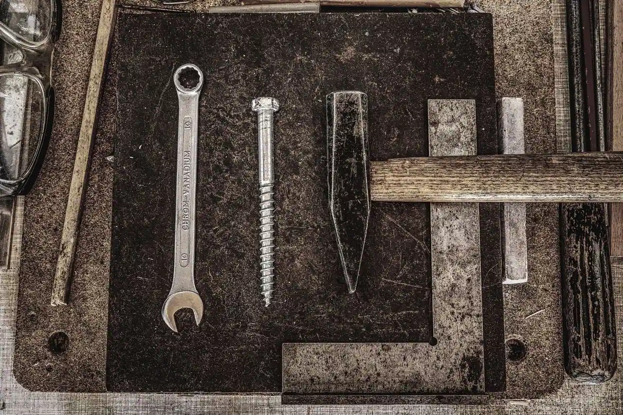 Outils à main — clé plate, vis, burin et marteau — posés sur un établi de bricolage patiné.