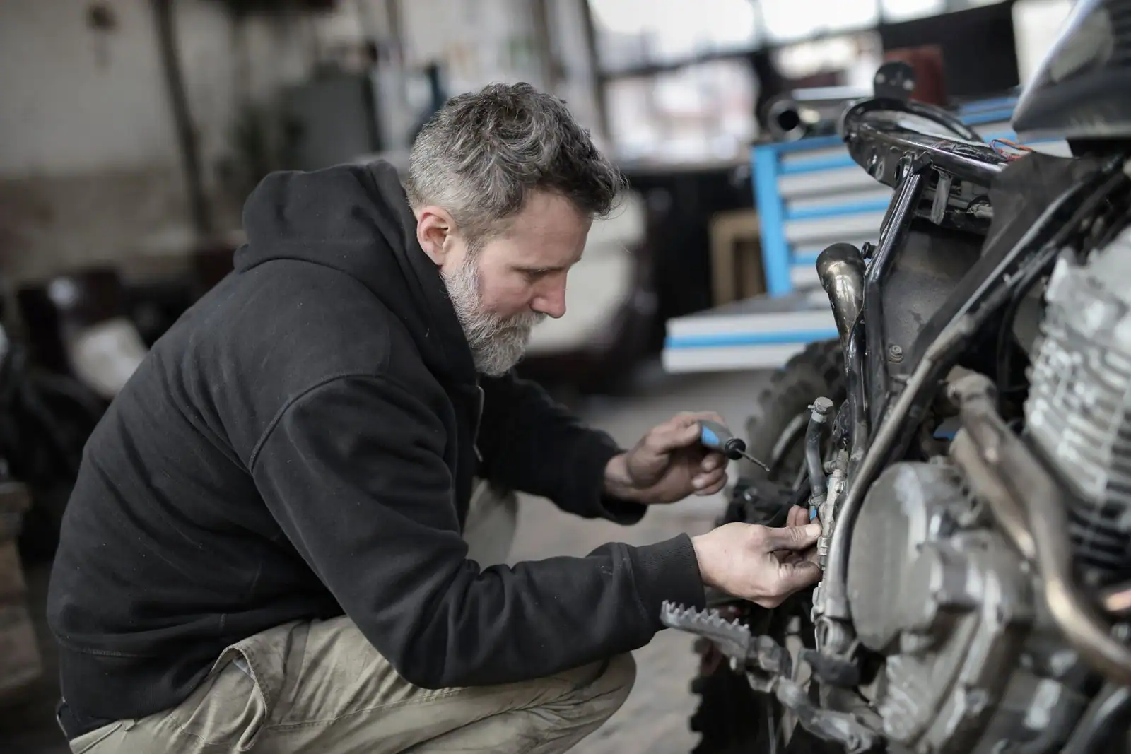 Mécanicien travaillant sur une moto tout-terrain dans un atelier, près de la roue arrière à pneu cranté.