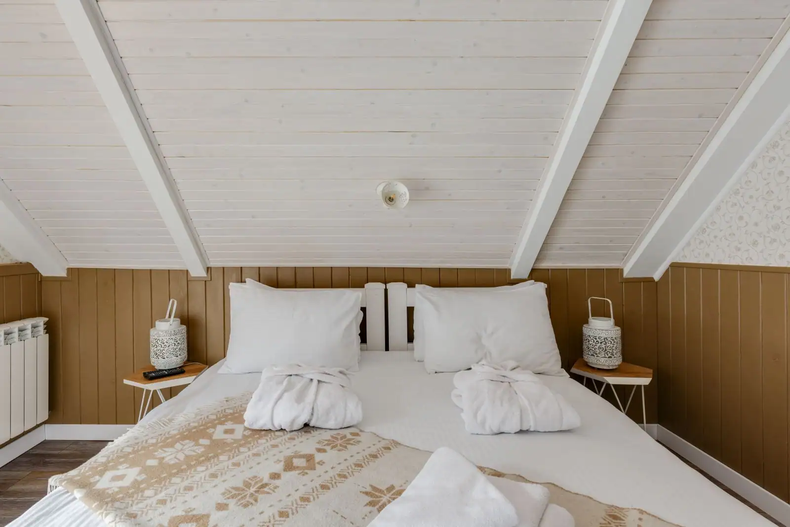 Chambre cocooning sous combles, murs lambrissés bois, lit blanc, plaid à motifs et lampes de chevet assorties
