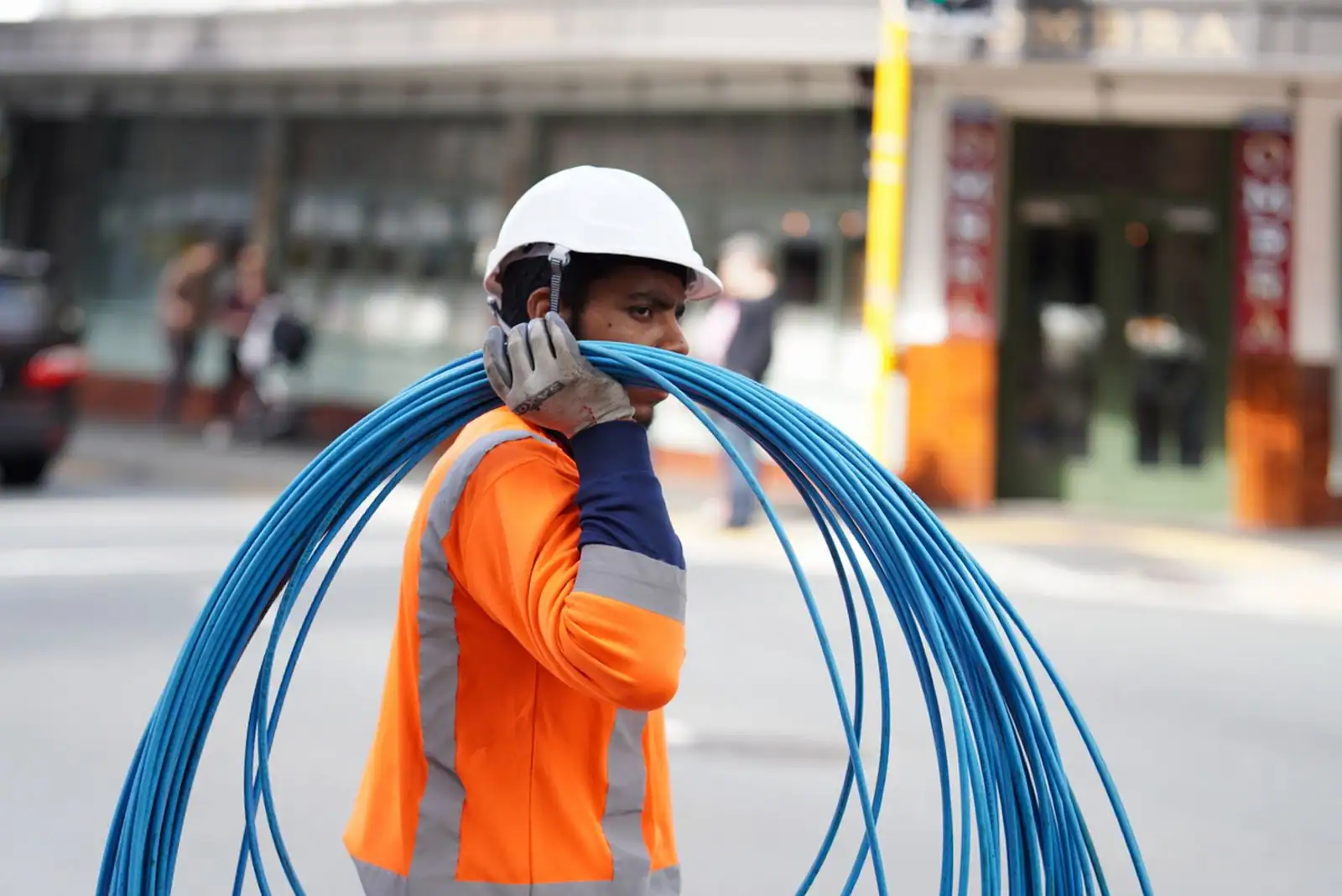 Technicien en gilet portant un rouleau de câbles réseau bleus en ville, évoquant le tirage de câbles télécom