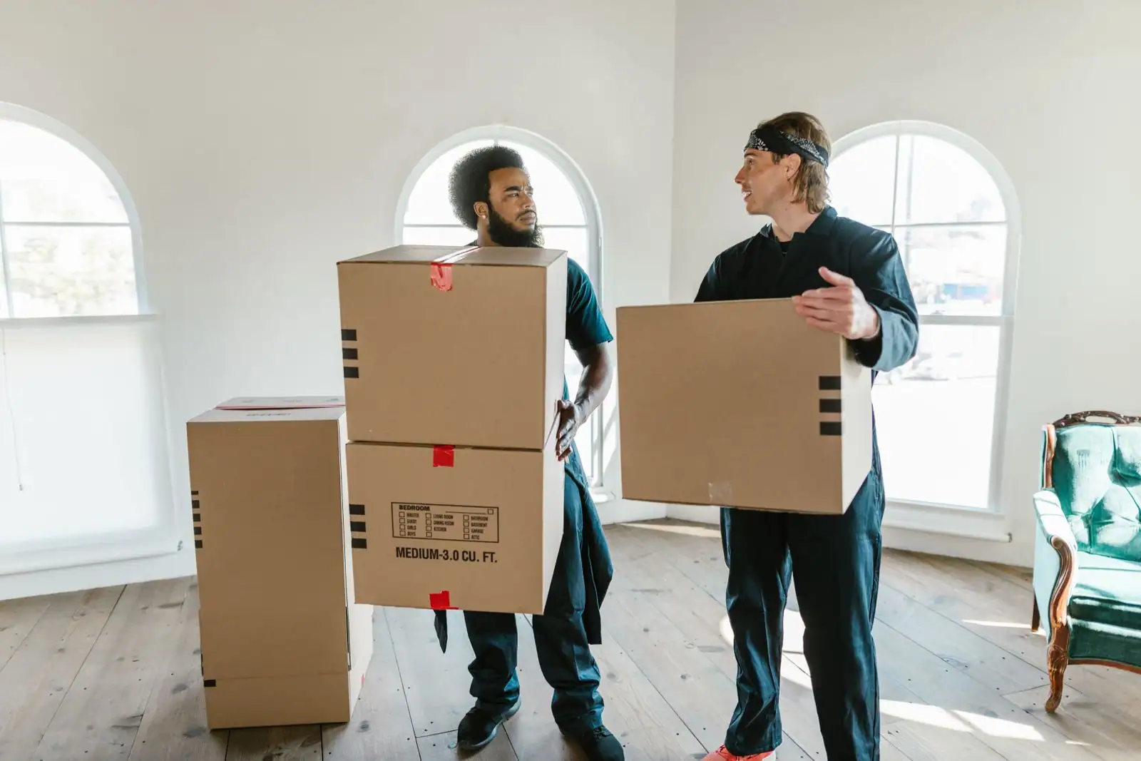 Deux déménageurs en tenue de travail portant des cartons dans une pièce lumineuse lors d'un déménagement
