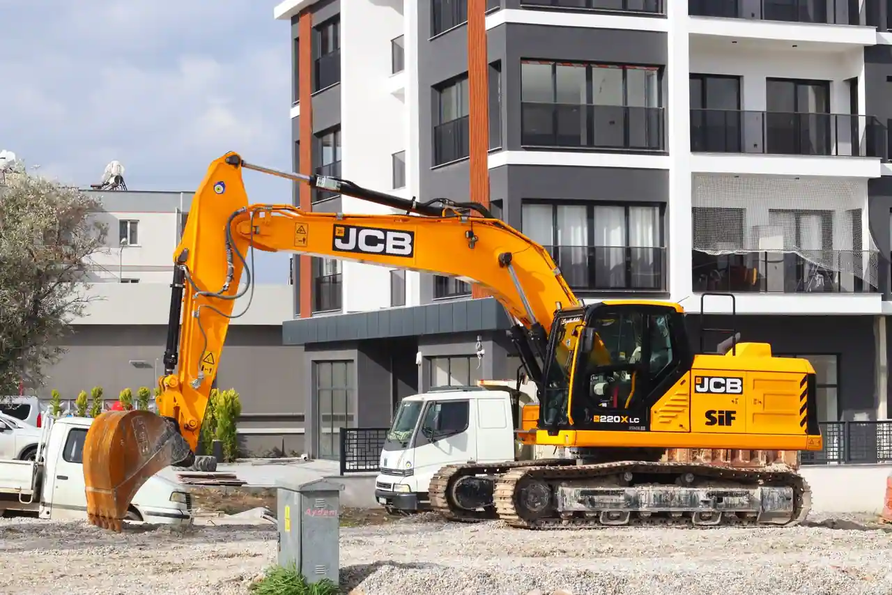 Pelleteuse jaune de marque JCB stationnée sur un chantier, devant un bâtiment en cours de finition.