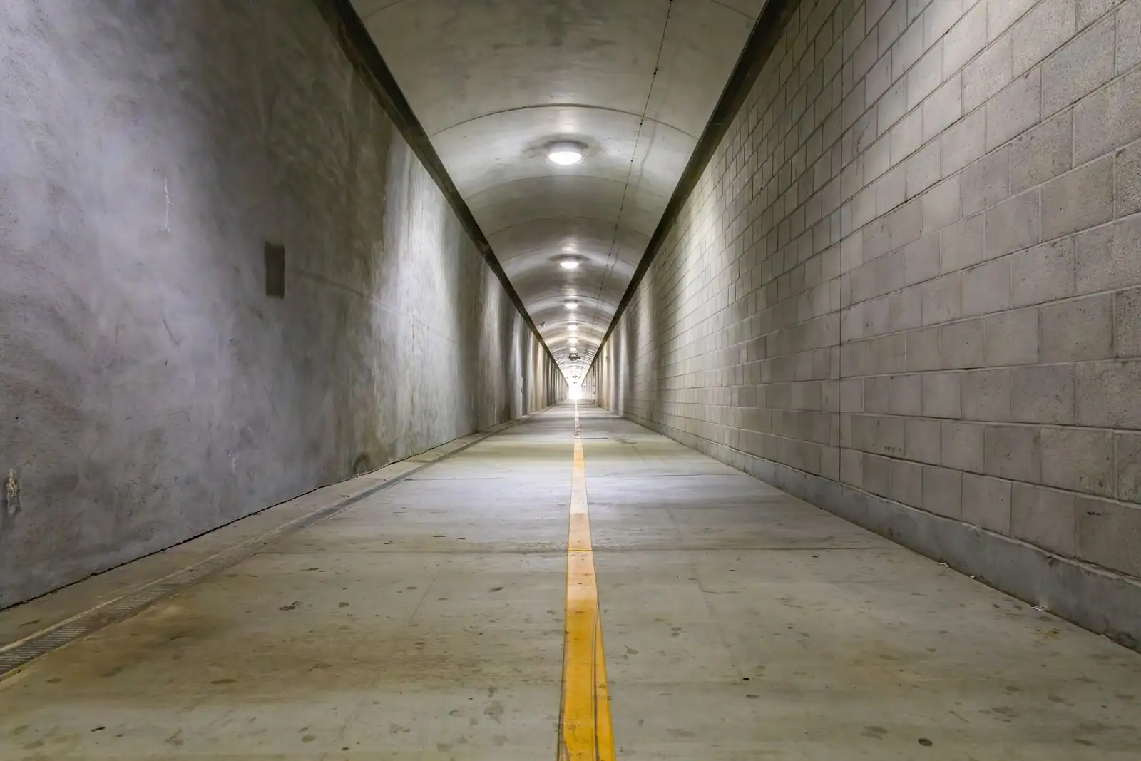 Intérieur d'un long tunnel souterrain bétonné et éclairé, fuyant vers l'horizon, évoquant un grand ouvrage de génie civil