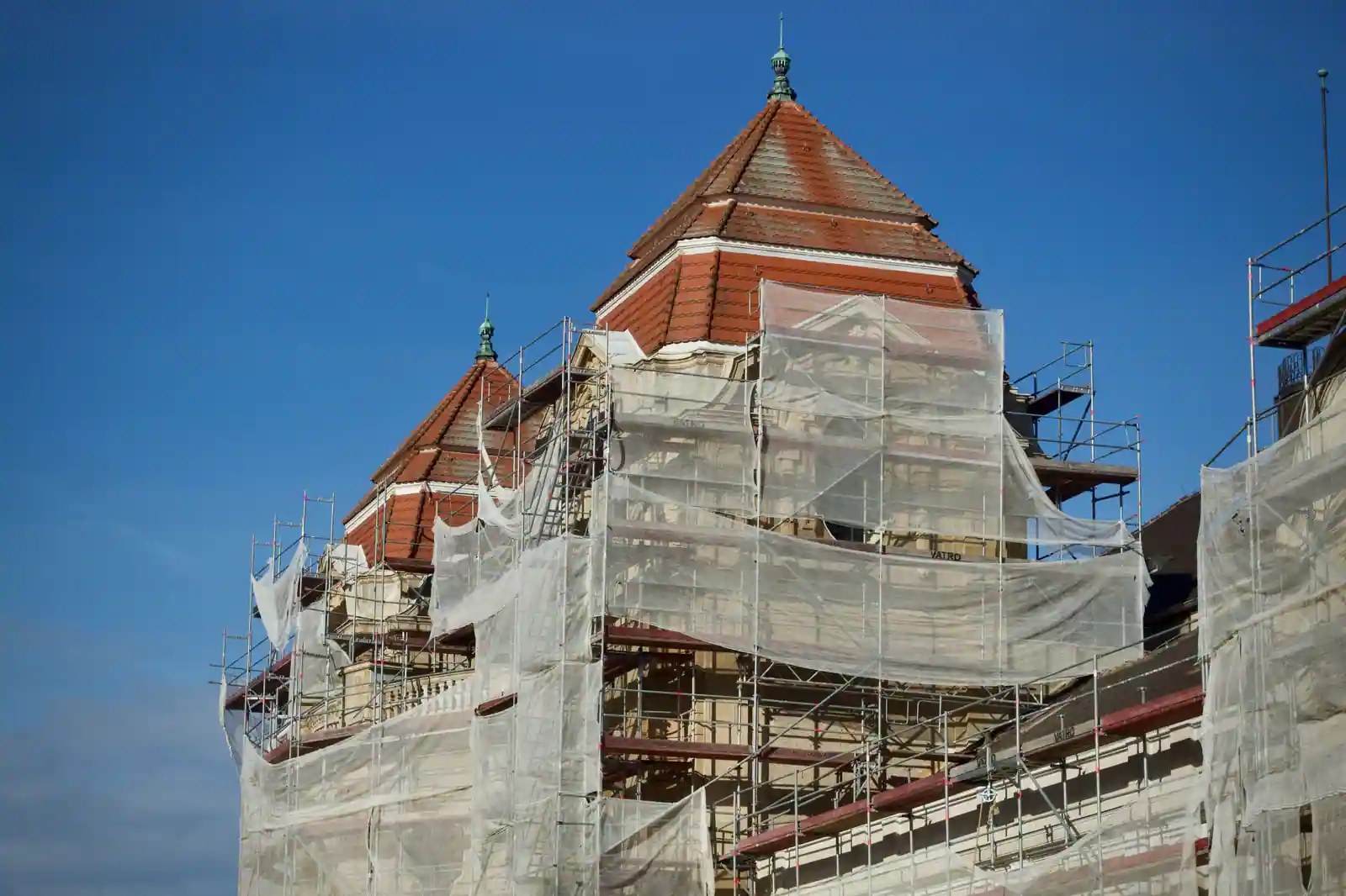 Bâtiment patrimonial en cours de restauration, couvert d'échafaudages et de bâches sous un ciel bleu