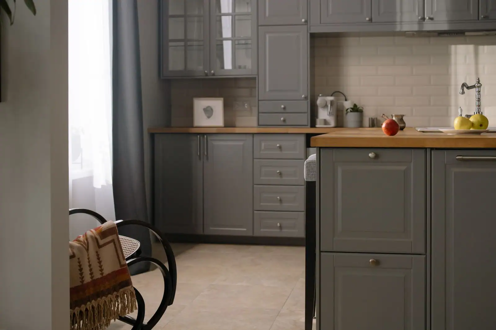 Cuisine aux façades grises avec crédence en carrelage blanc et plan de travail en bois.