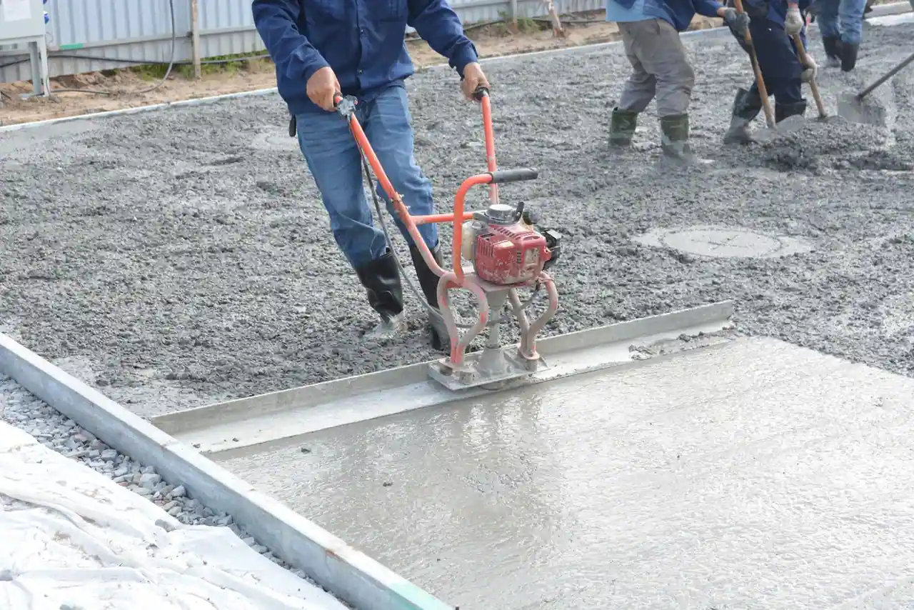 Ouvriers nivelant une dalle de béton fraîchement coulée avec une règle vibrante sur un chantier.