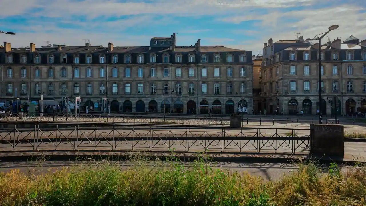Façades de pierre du XVIIIe siècle et voies de tramway sur les quais de Bordeaux, sous un ciel clair.