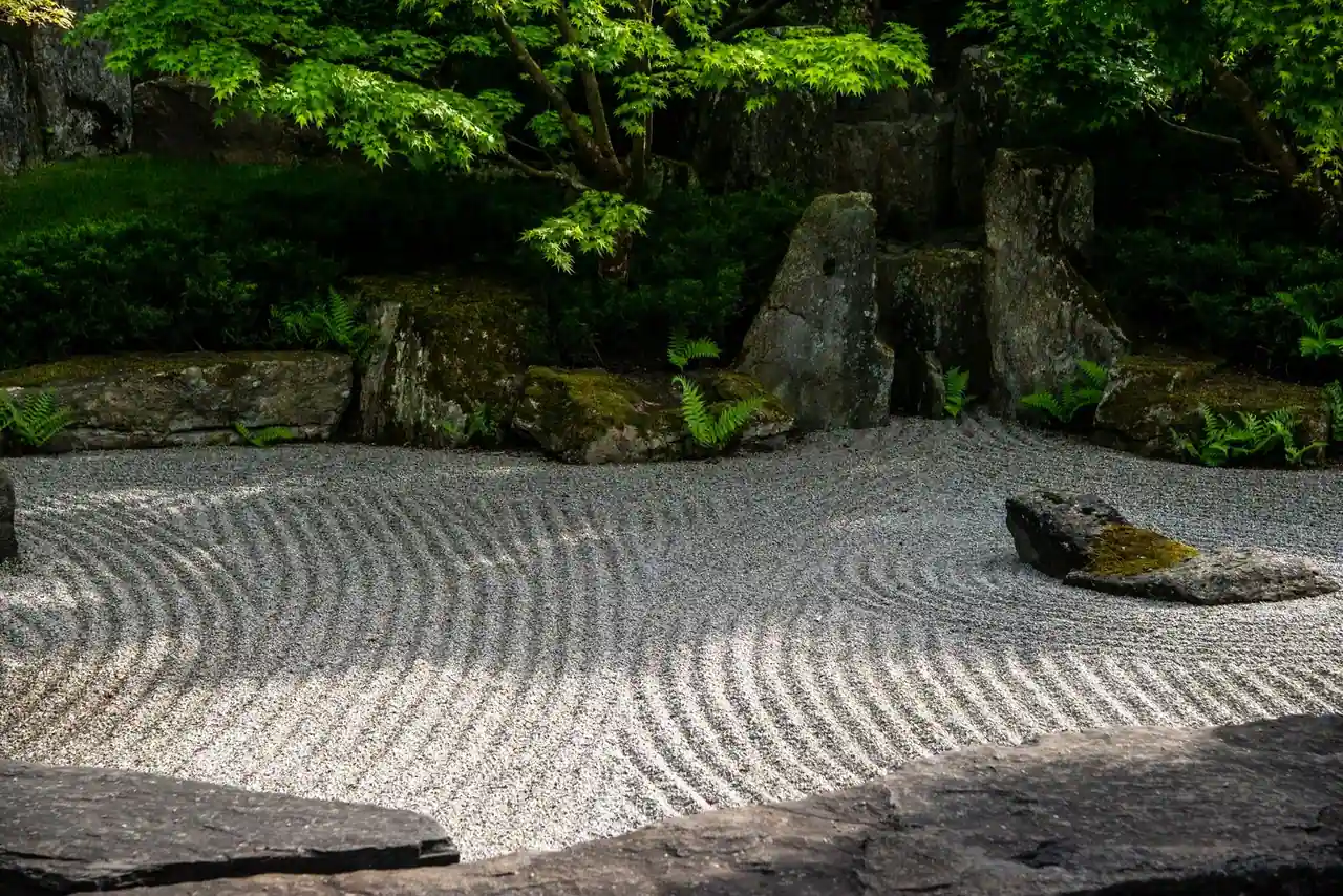 Jardin zen japonais avec gravier clair ratissé, pierres posées et coussins de mousse