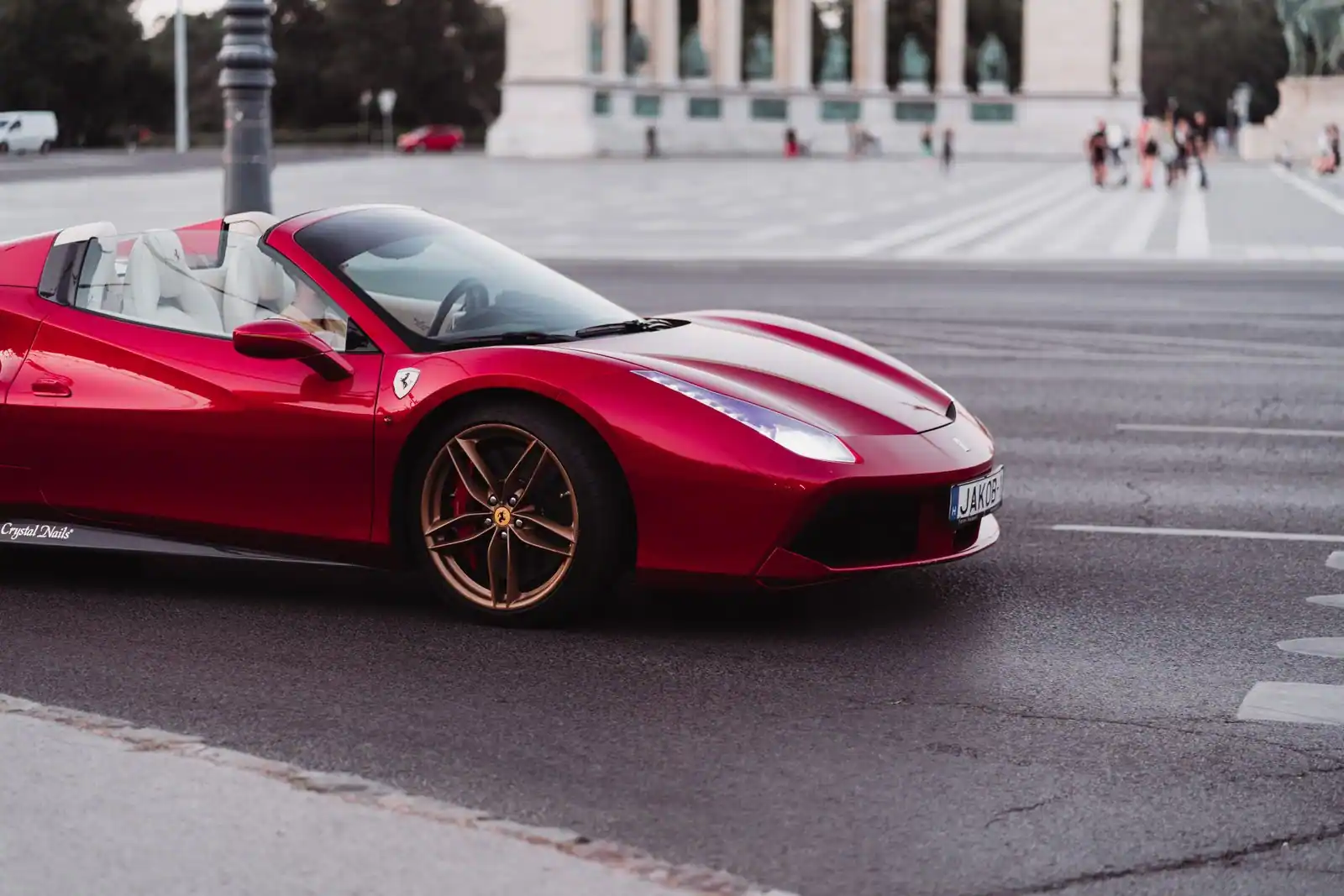 Ferrari de sport rouge décapotable roulant en ville, carrosserie basse aux lignes tendues.