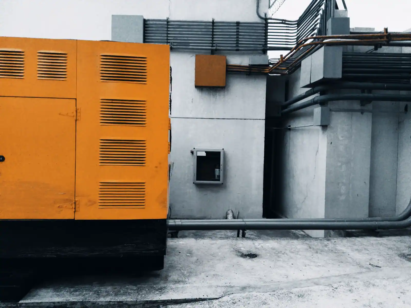 Groupe électrogène industriel sous capot orange installé à l'extérieur contre un bâtiment en béton.
