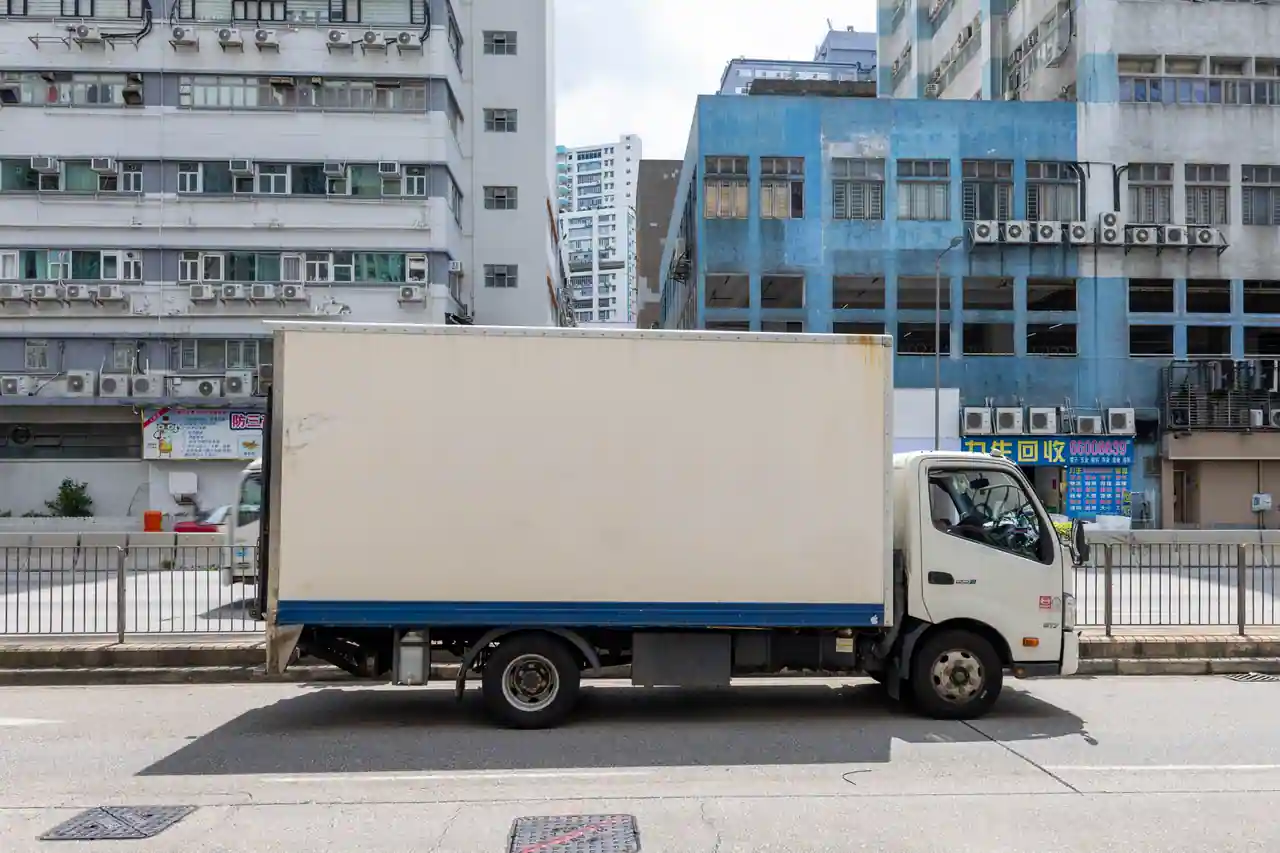 Camion utilitaire à caisse blanche stationné le long d'une rue, prêt pour un déménagement.