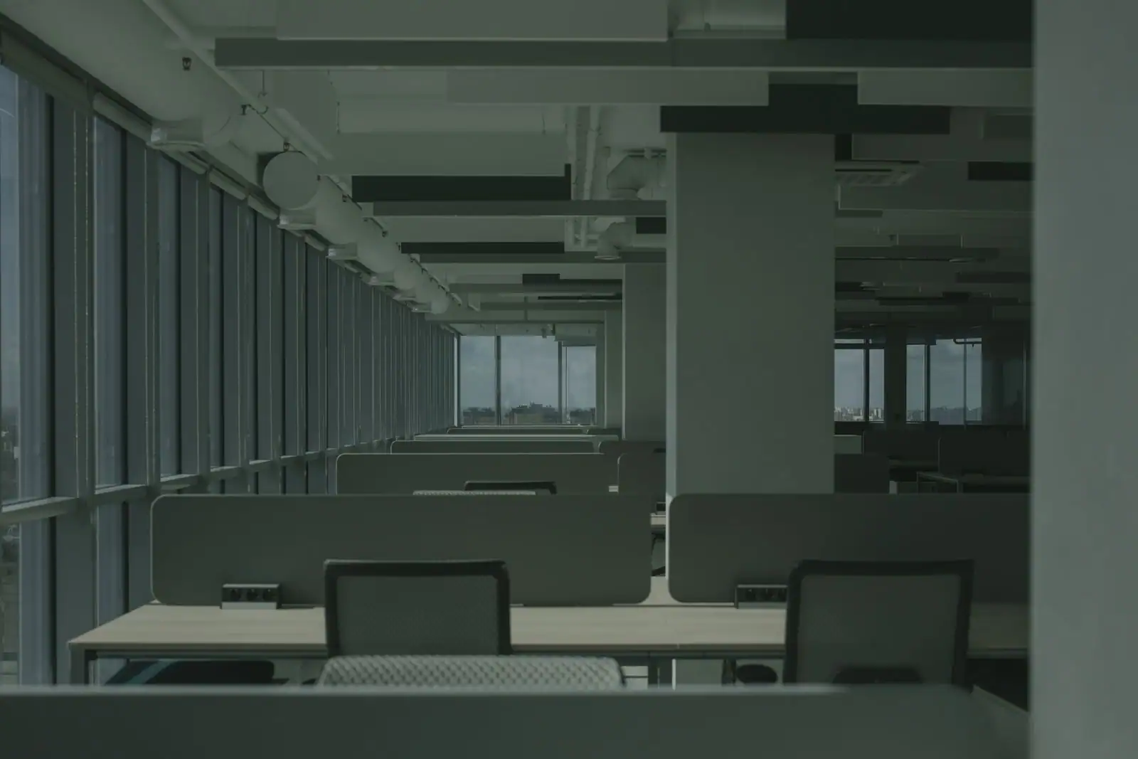 Plateau de bureaux vide avec postes de travail, cloisons basses et grandes baies vitrées donnant sur la ville.