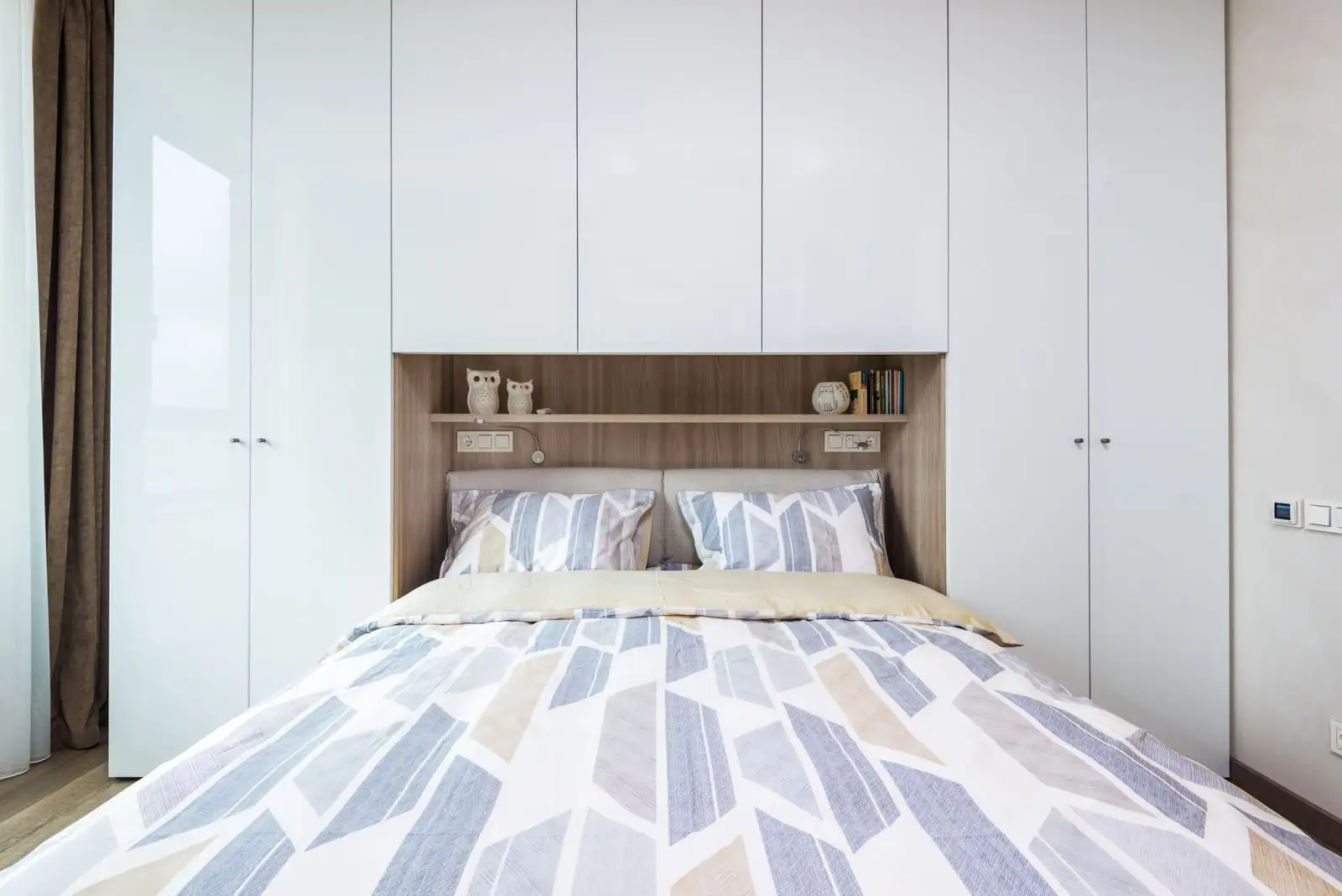 Chambre avec placards blancs sur mesure intégrés du sol au plafond, autour d'une tête de lit en bois clair à étagère