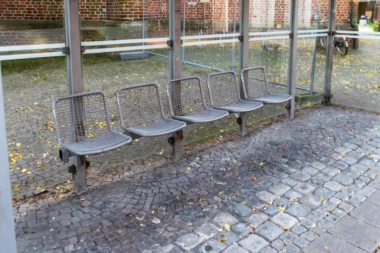 Sièges individuels en métal séparés dans un abribus vitré, empêchant de s'allonger dans l'espace public.