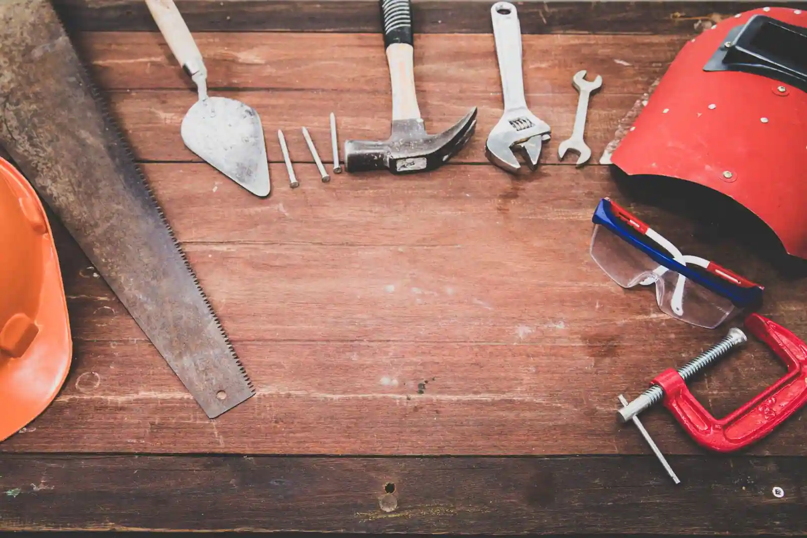 Outils de bricolage sur une table en bois : scie, marteau, clés, clou, serre-joint et casque de chantier.