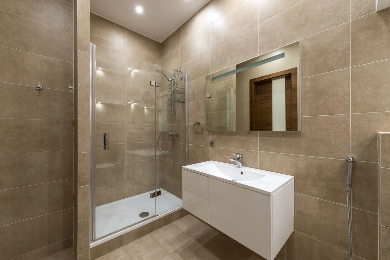 Salle de bain rénovée avec douche vitrée à l'italienne, meuble vasque et carrelage beige.