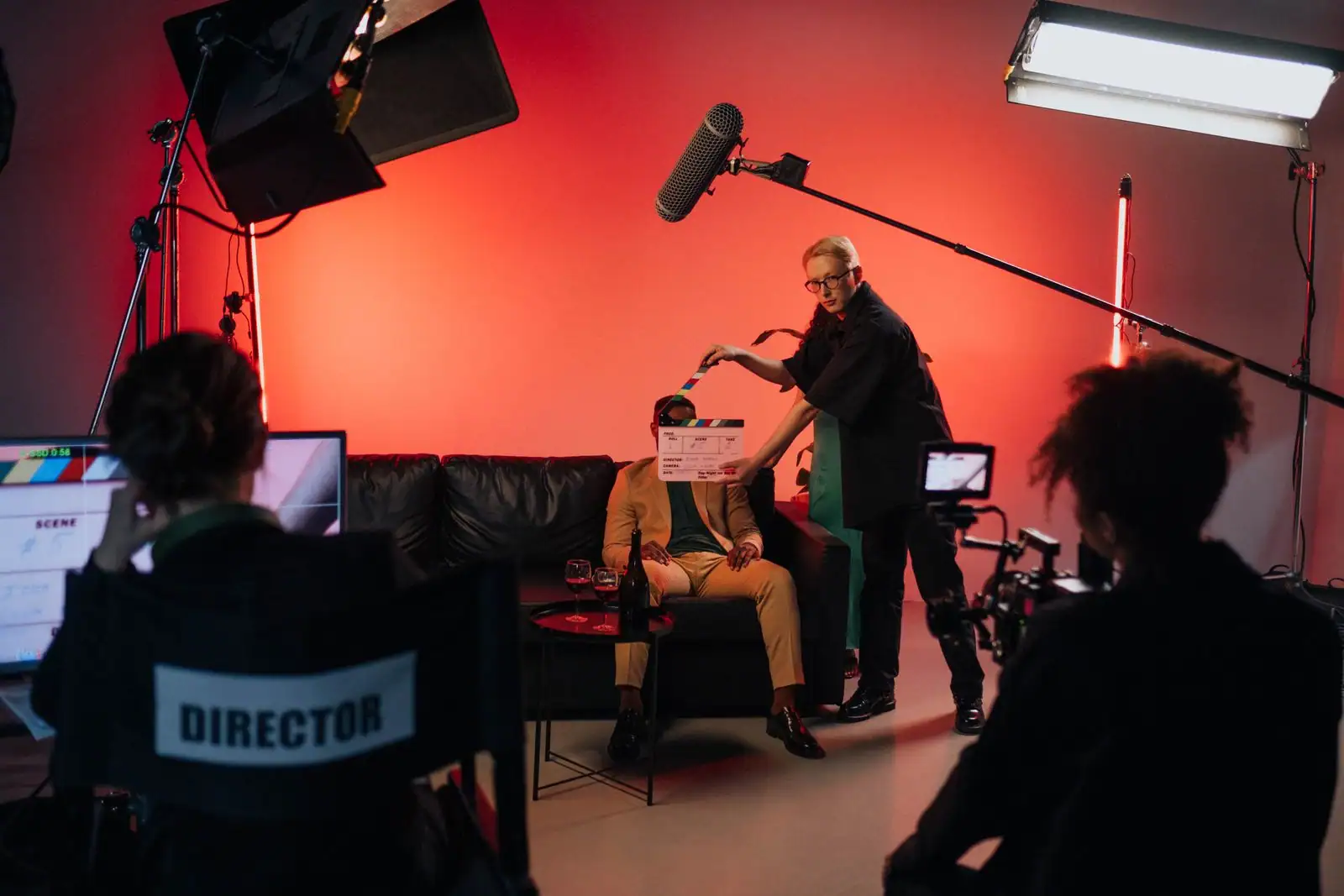 Tournage de film : un clap présenté devant un acteur assis sur un canapé, sous les projecteurs et la perche son.
