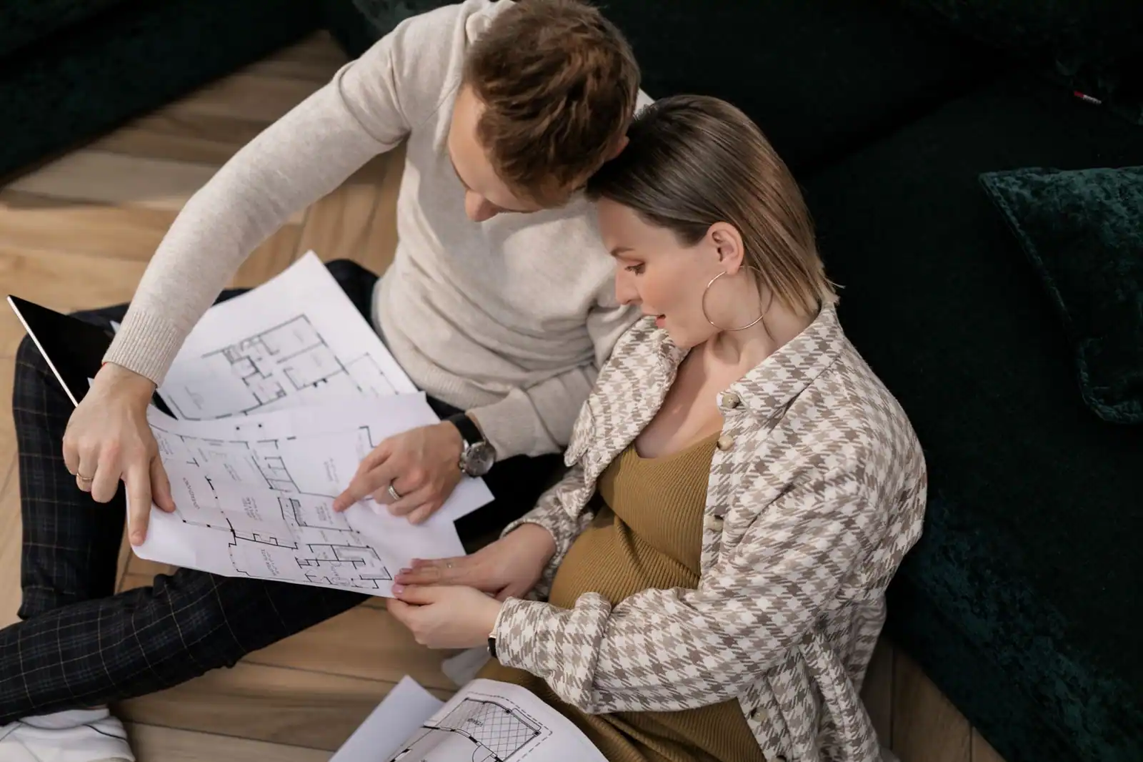 Un couple assis au sol de son salon étudie le plan de la pièce, canapé et tablette à portée de main