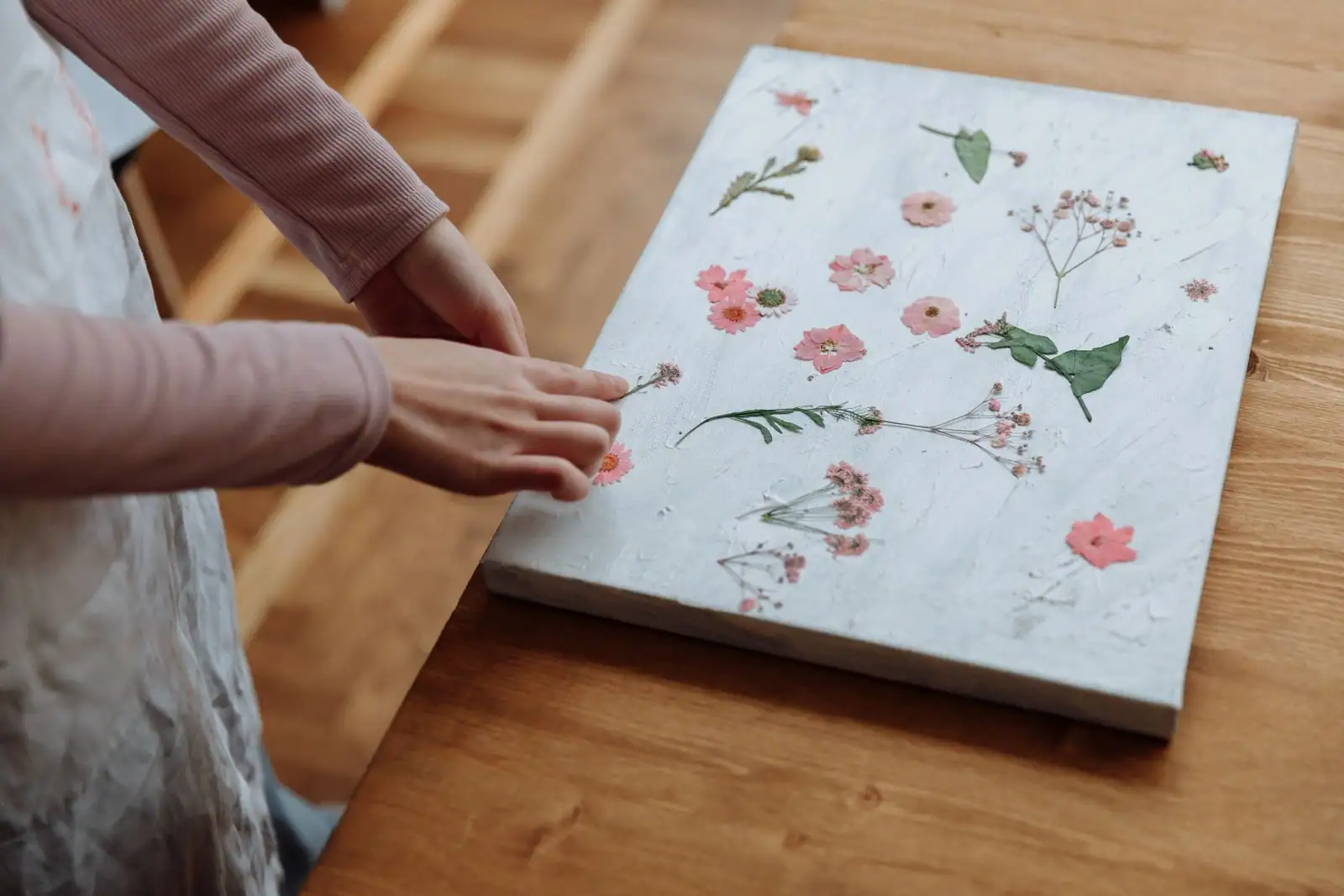 Mains disposant des fleurs et des feuilles séchées sur un support clair, sur une table en bois