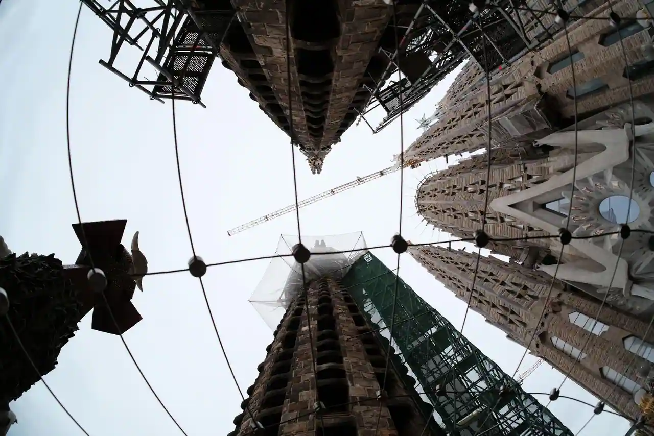 Contre-plongée sur les tours de la Sagrada Família à Barcelone, entre grue de chantier et échafaudages.