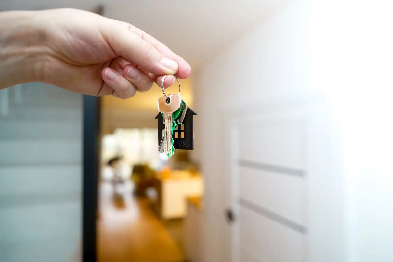 Main tenant une clé de logement et son porte-clés en forme de maison, devant l'entrée d'un appartement