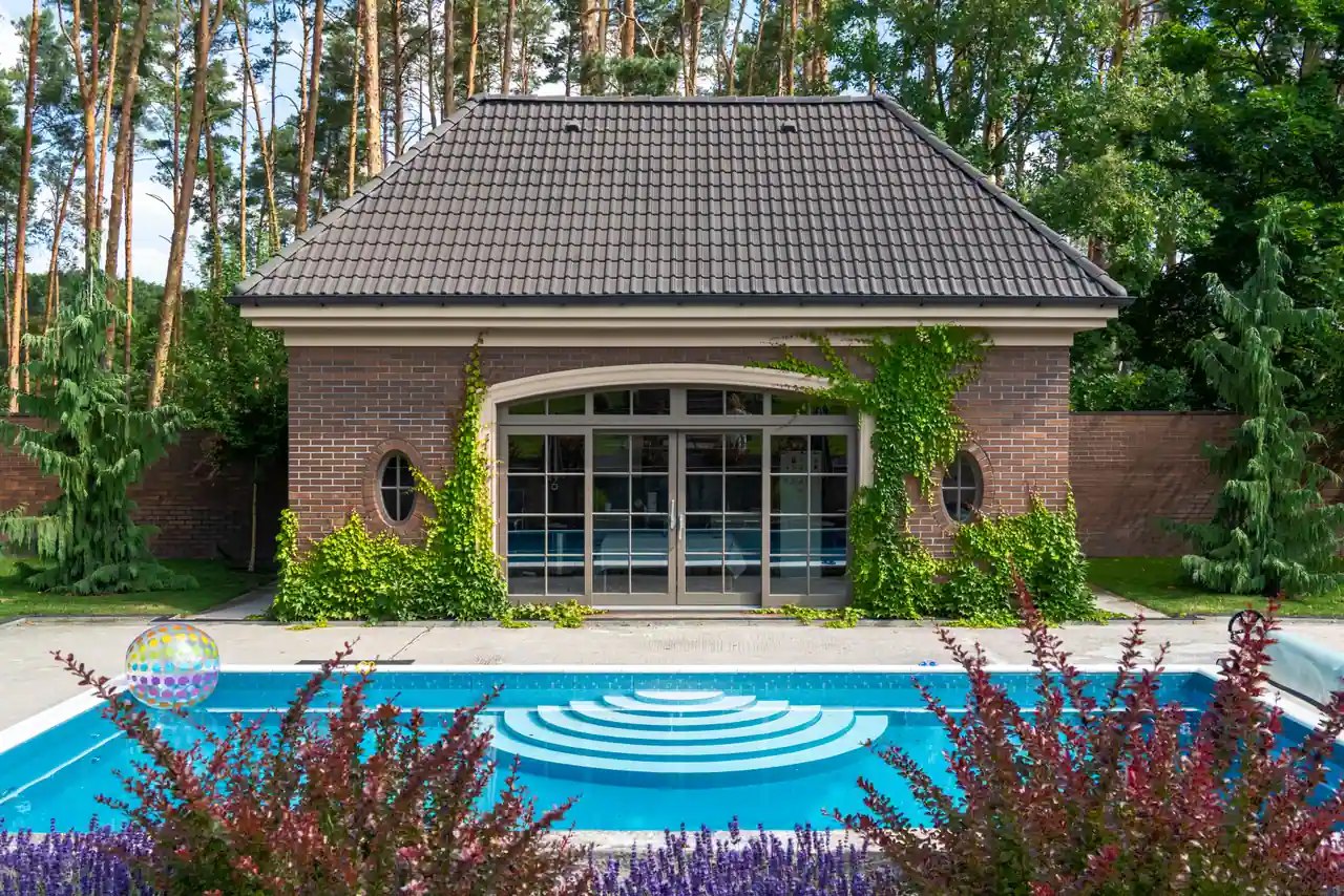 Piscine extérieure dans un jardin clos de murs en brique, bordée de massifs, sous une lumière douce